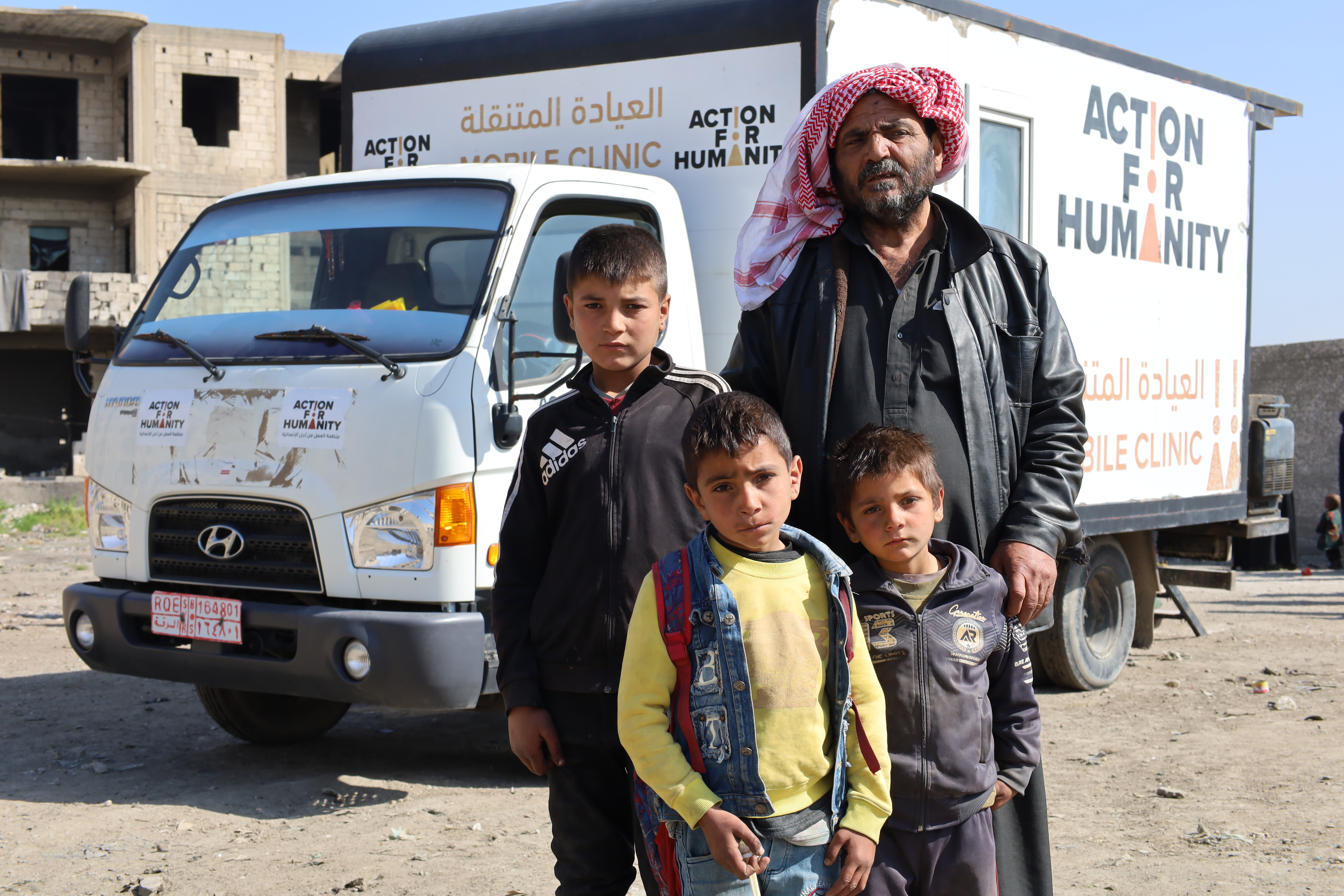 Haitham and his three children next to the AFH mobile clinic