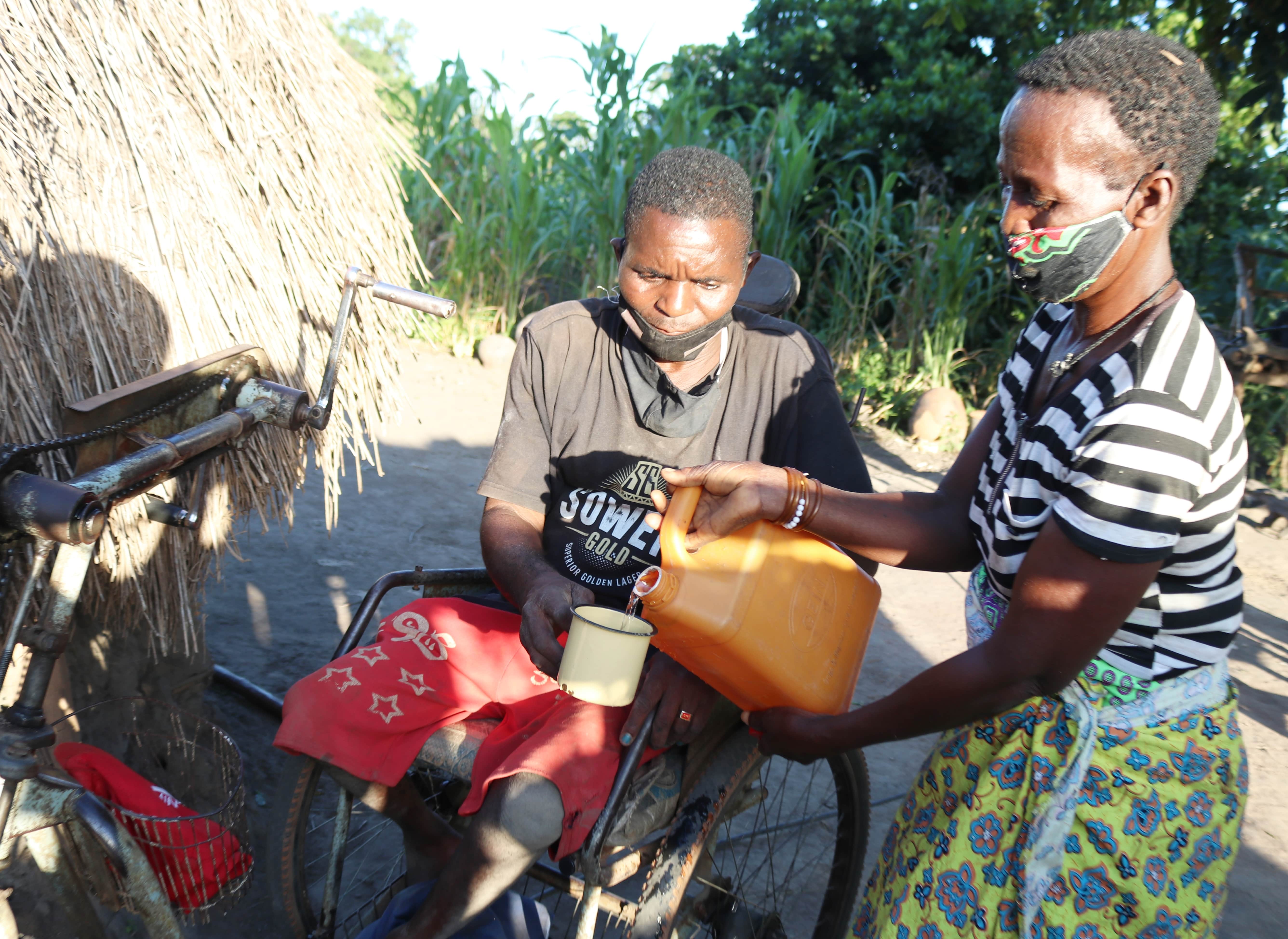 In front of their house built with frigile local materials, Celeste is filling a cup with clean water so David can drink 