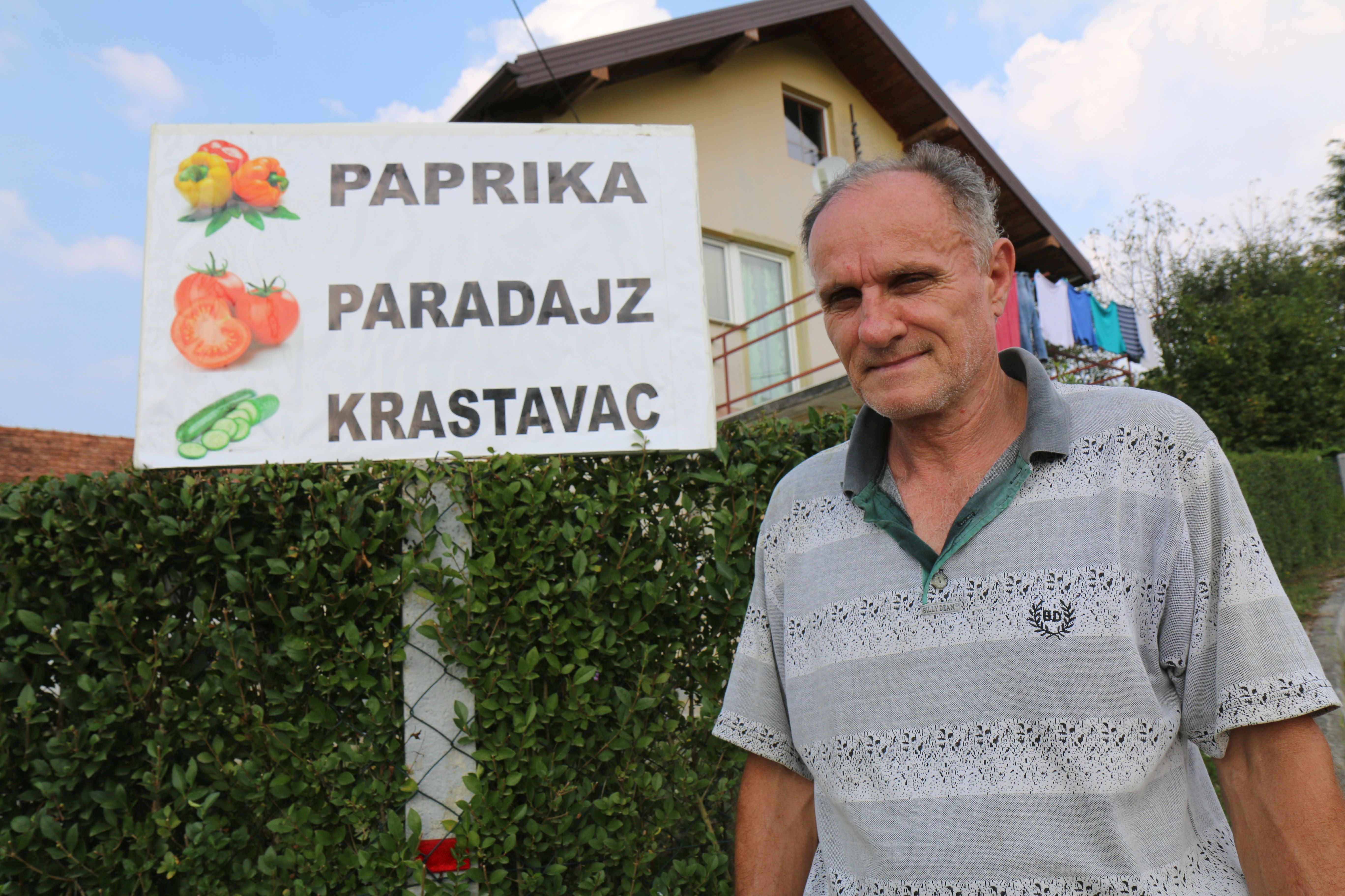 Dragan, landmine survivor, poses next to the sign announcing “vegetables for sale”.