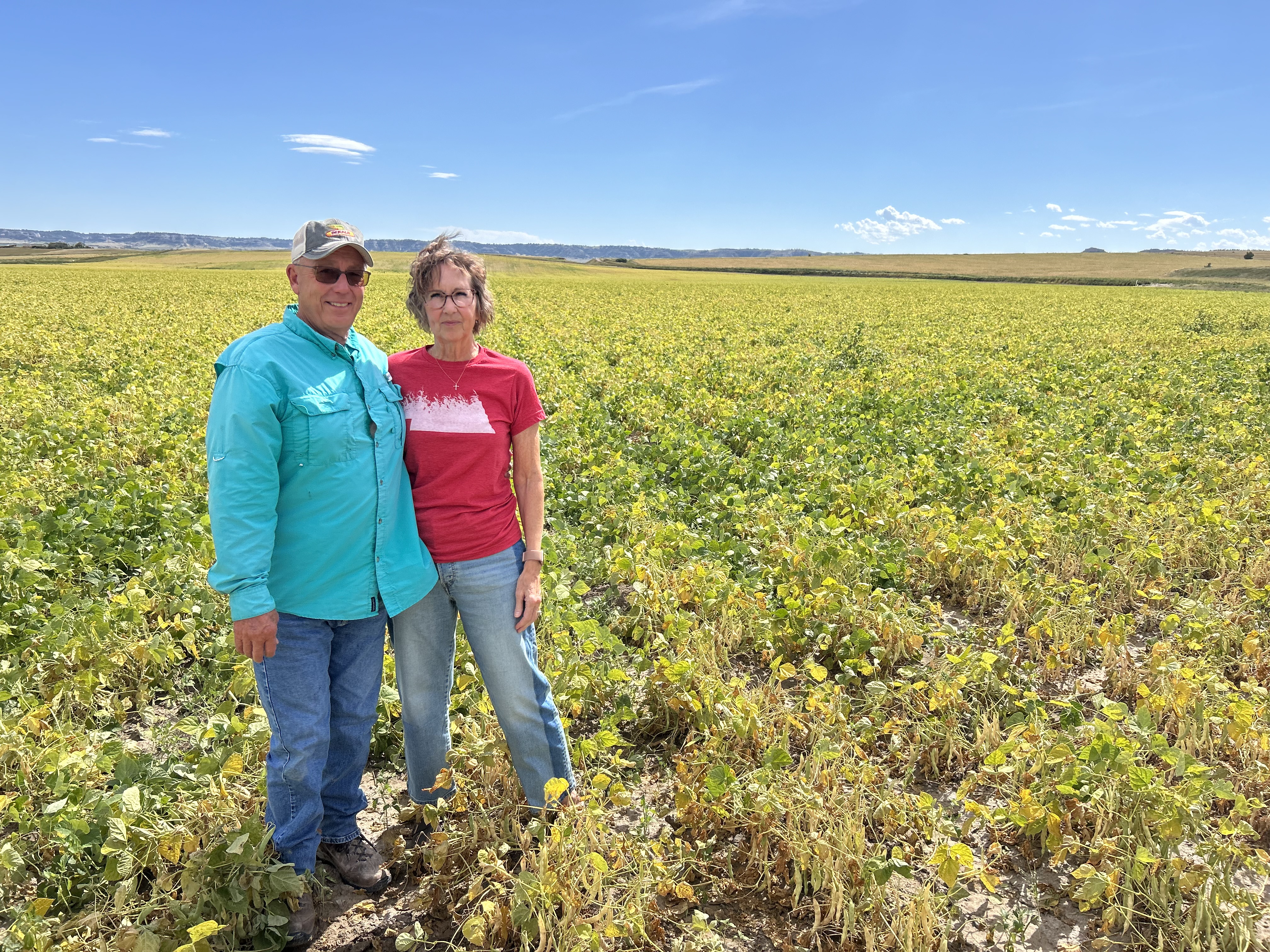A man and woman stand together in a field on their farm.