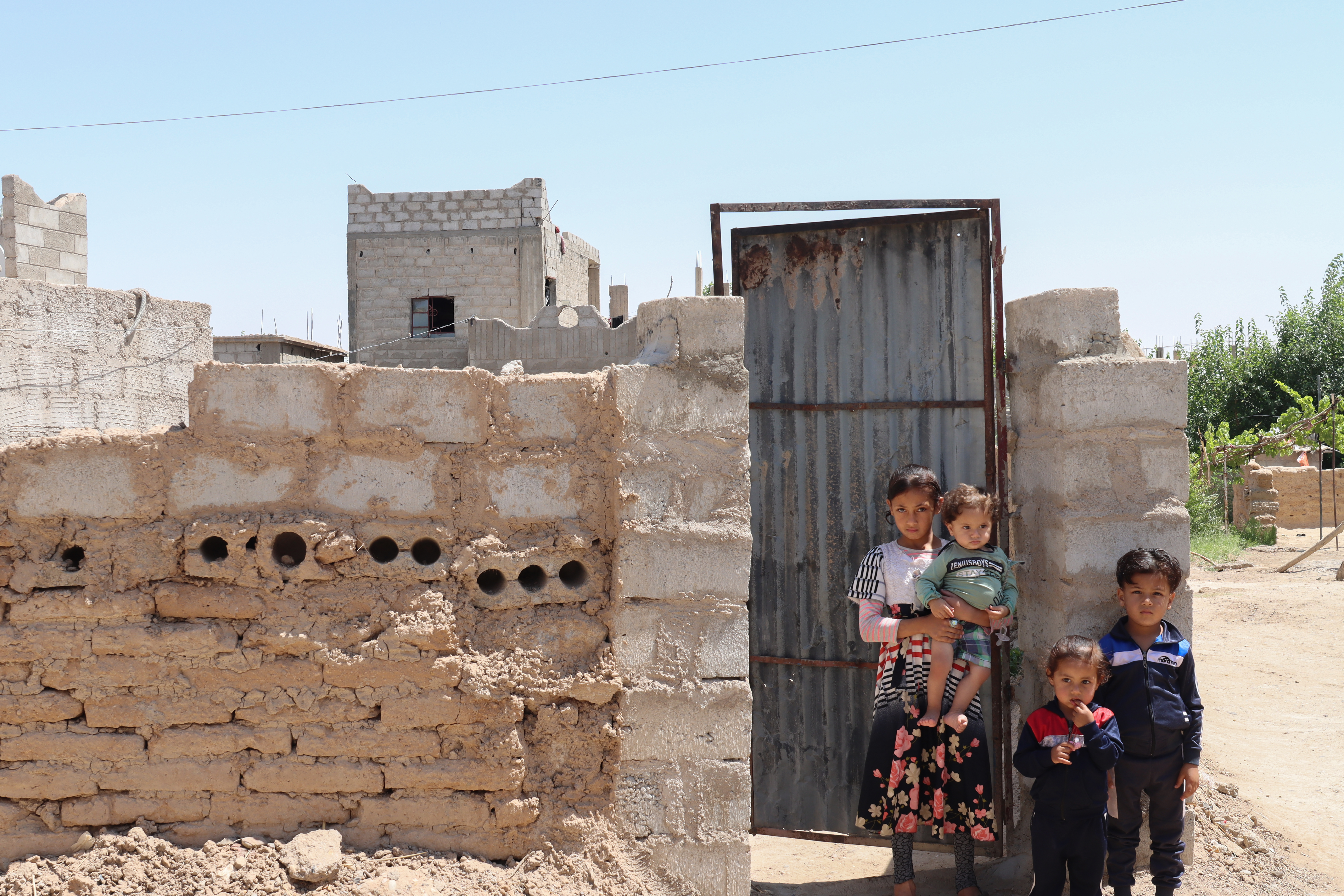 Khloud’s* children standing in front of their collapsing home in Syrian