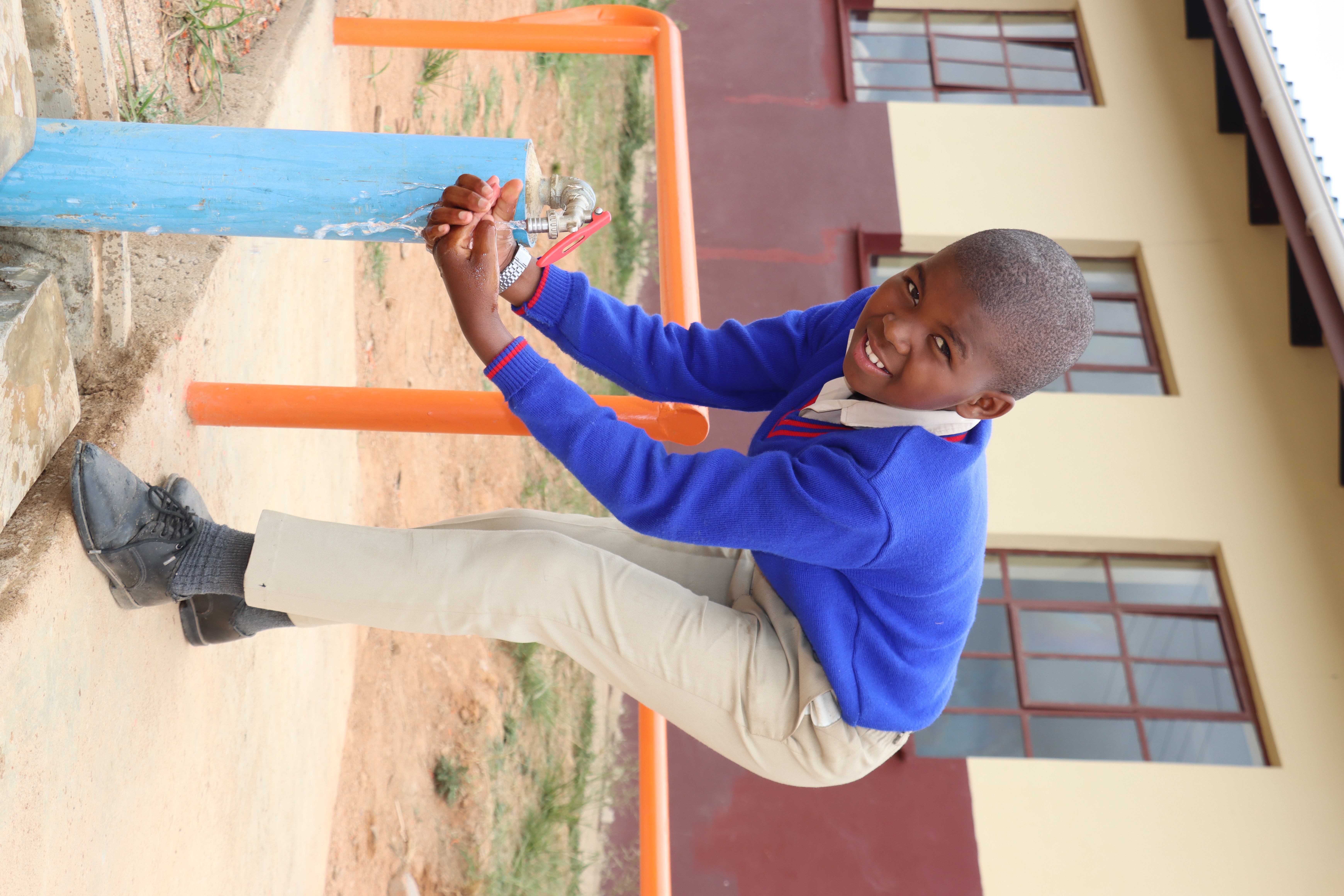 A learner washing hands from a tap inside a school.