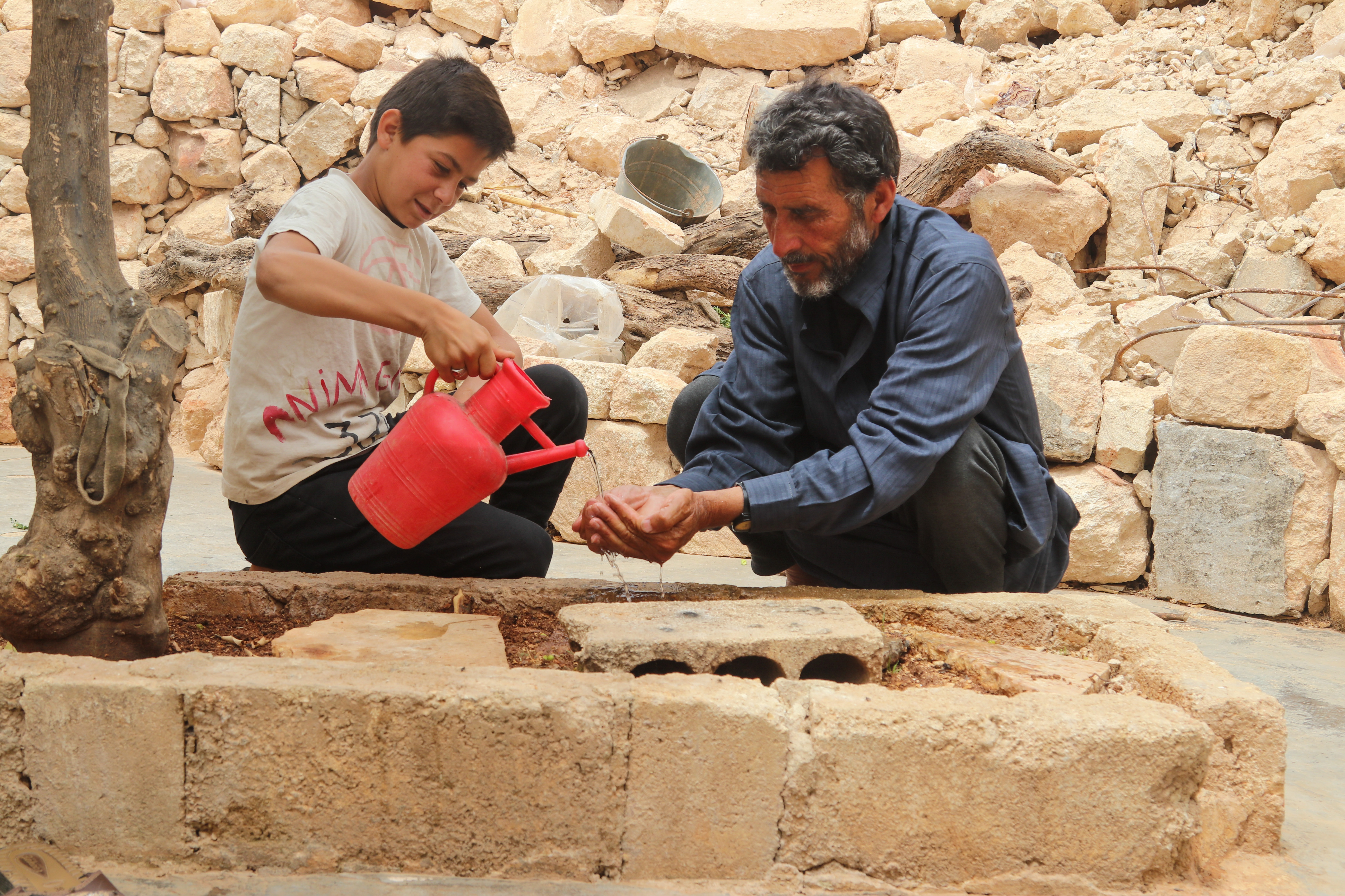 World Vision Syria Response Partner, ULUSLARARASI INSANI YARDIMLAŞMA DERNEĞI Abu Hashim’s grandchild helping him wash his hand.