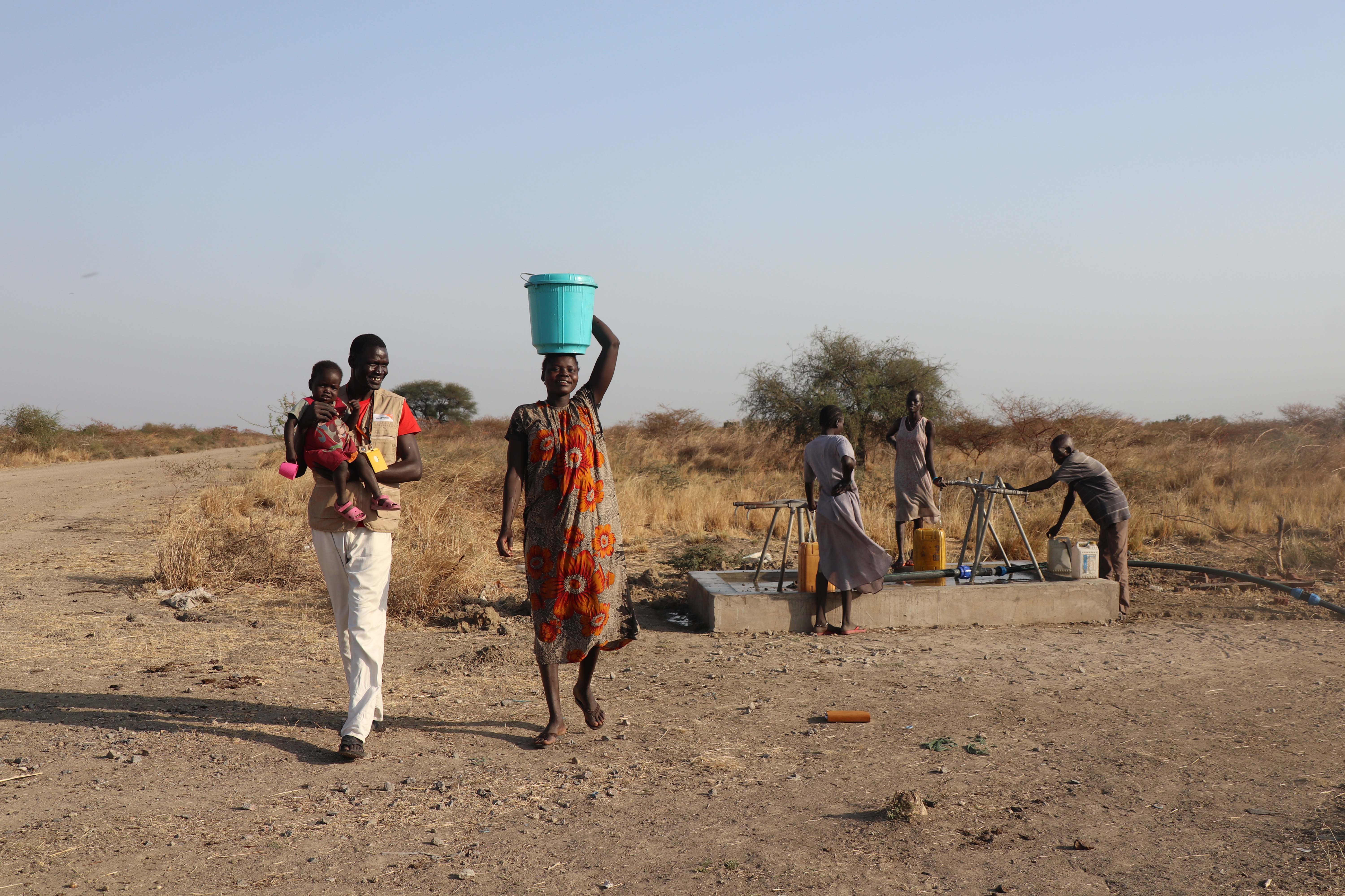 Nyathak walking with her child and WV staff from the water point by the roadside.