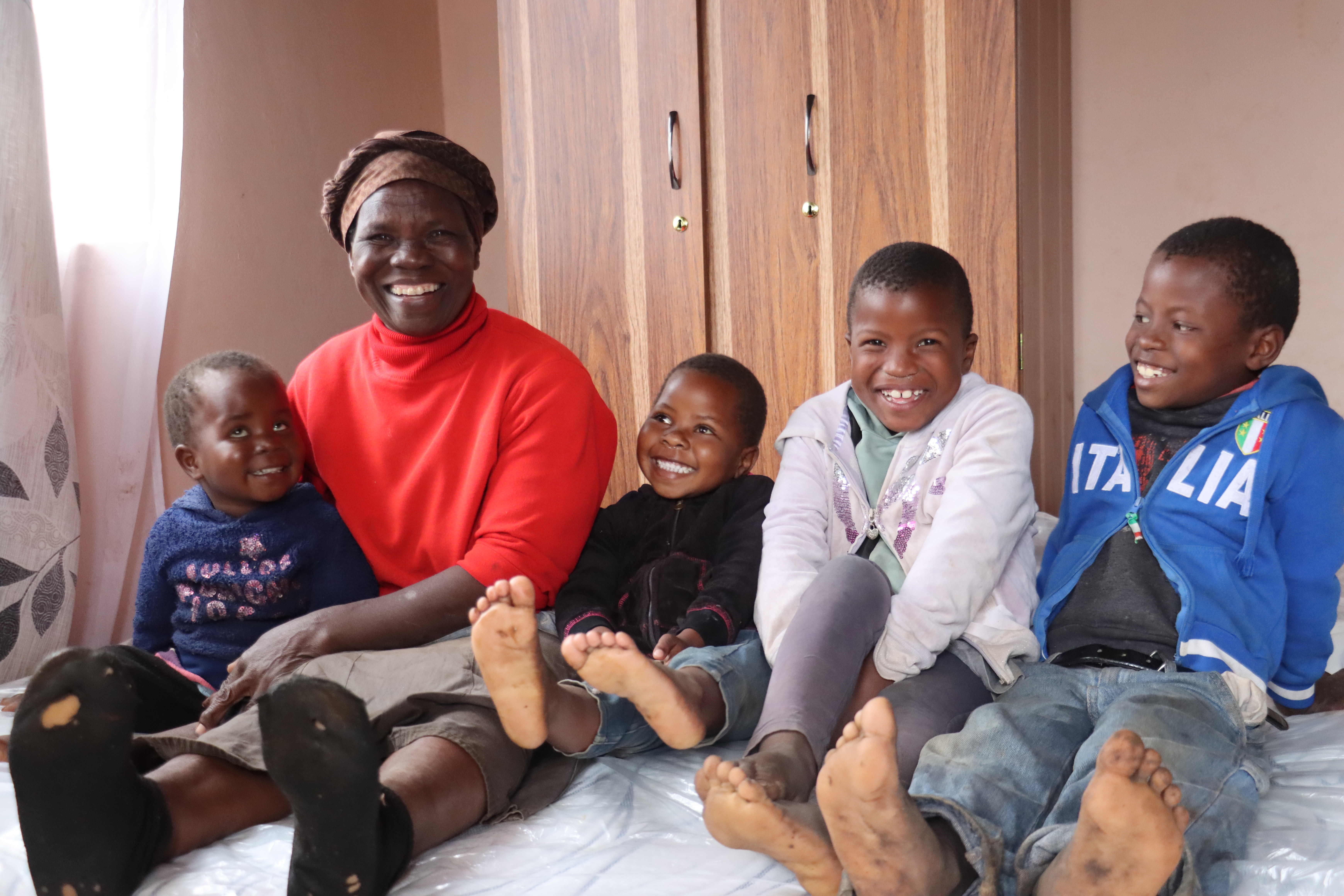 Linah Bhembe and her grandchildren sitting on a mattrass they reeived through World Vision's GIK Programme.