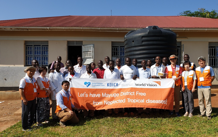 A large group of staff stand together holding a sign that says "Let's have Mayuge District Free from Neglected Tropical Diseases!"