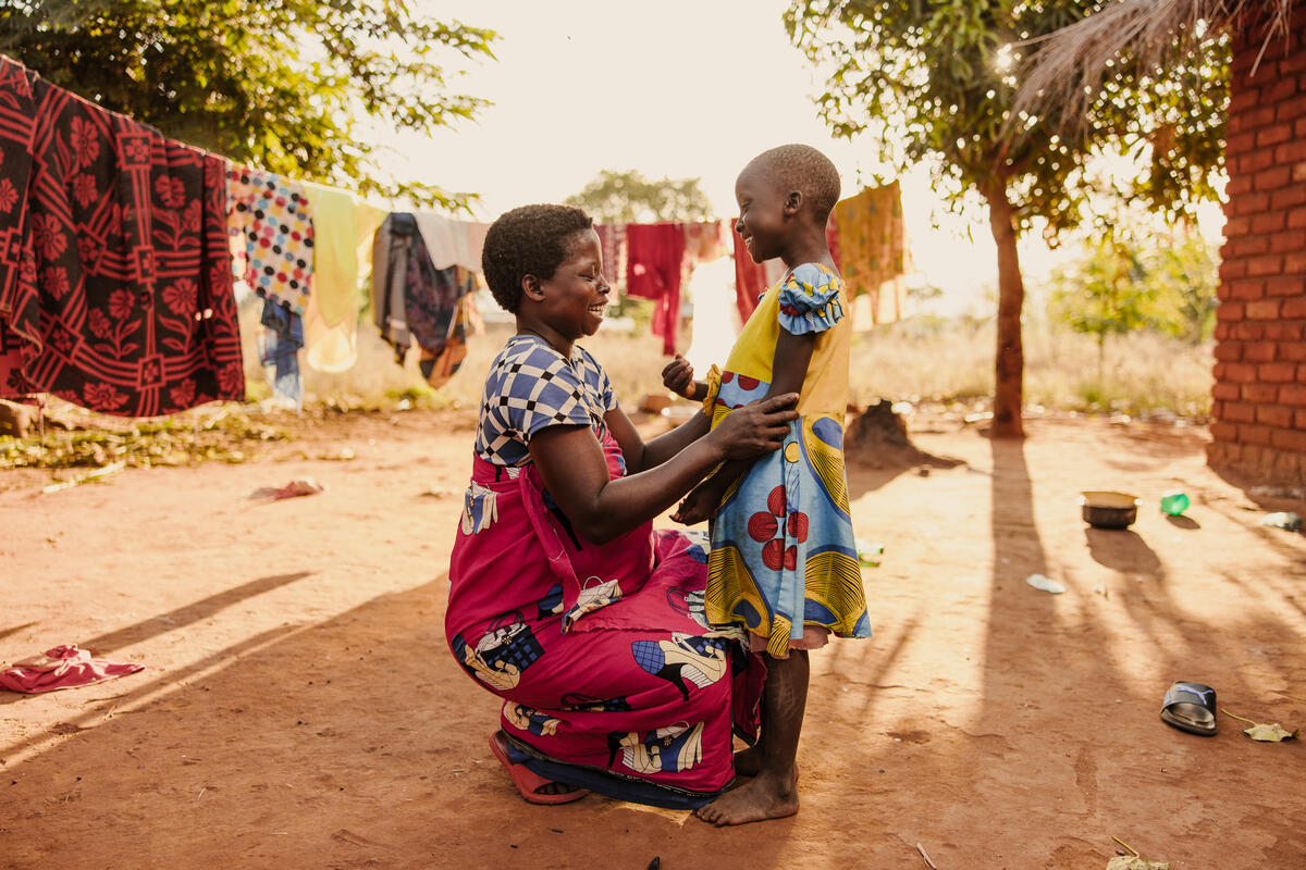 Mother looks at and speaks with a young child outside their home in Malawi