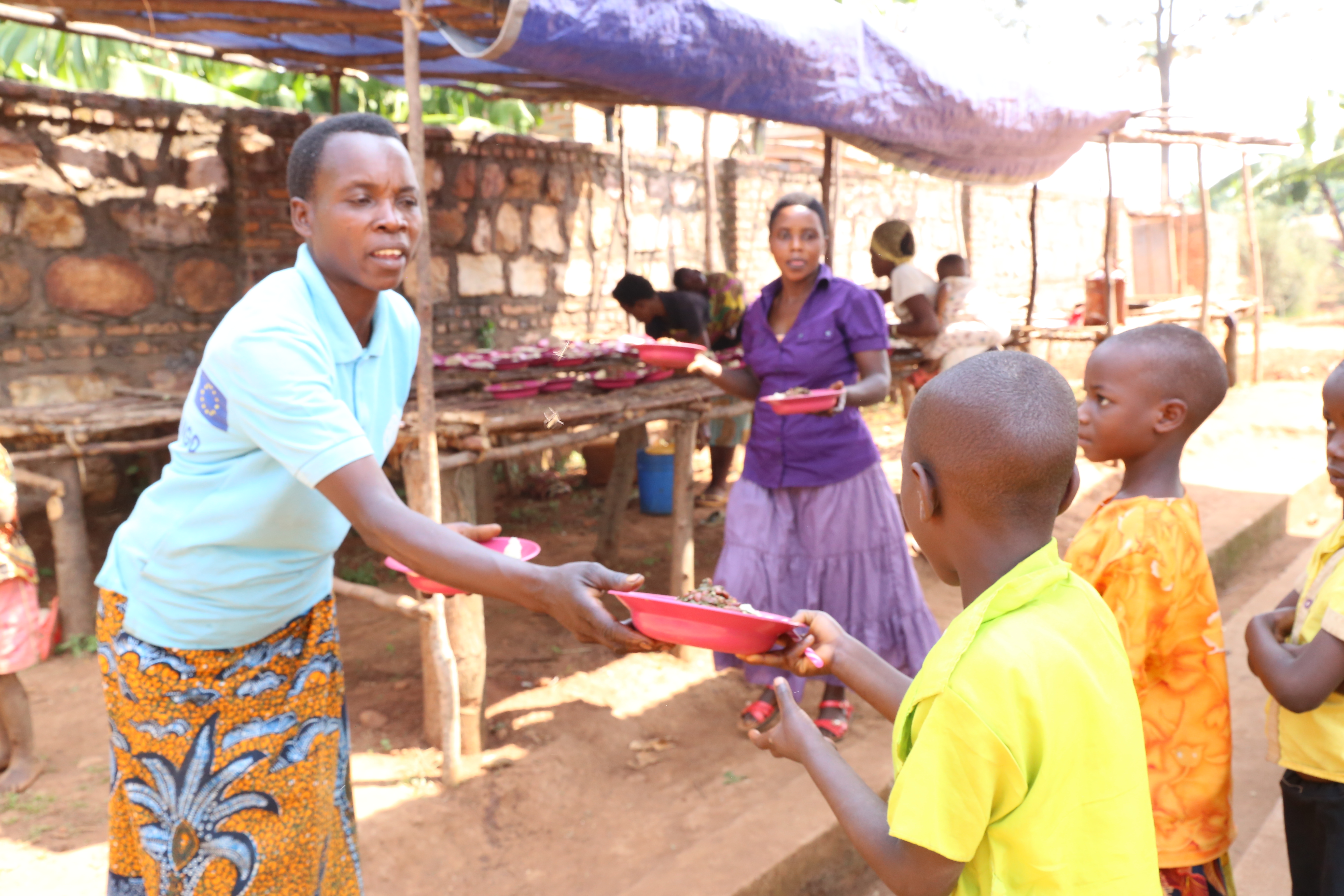 Clemence, a volunteer, serving food to children benefiting from a school canteen at Mwakiro II/World Vision/Javan/2021
