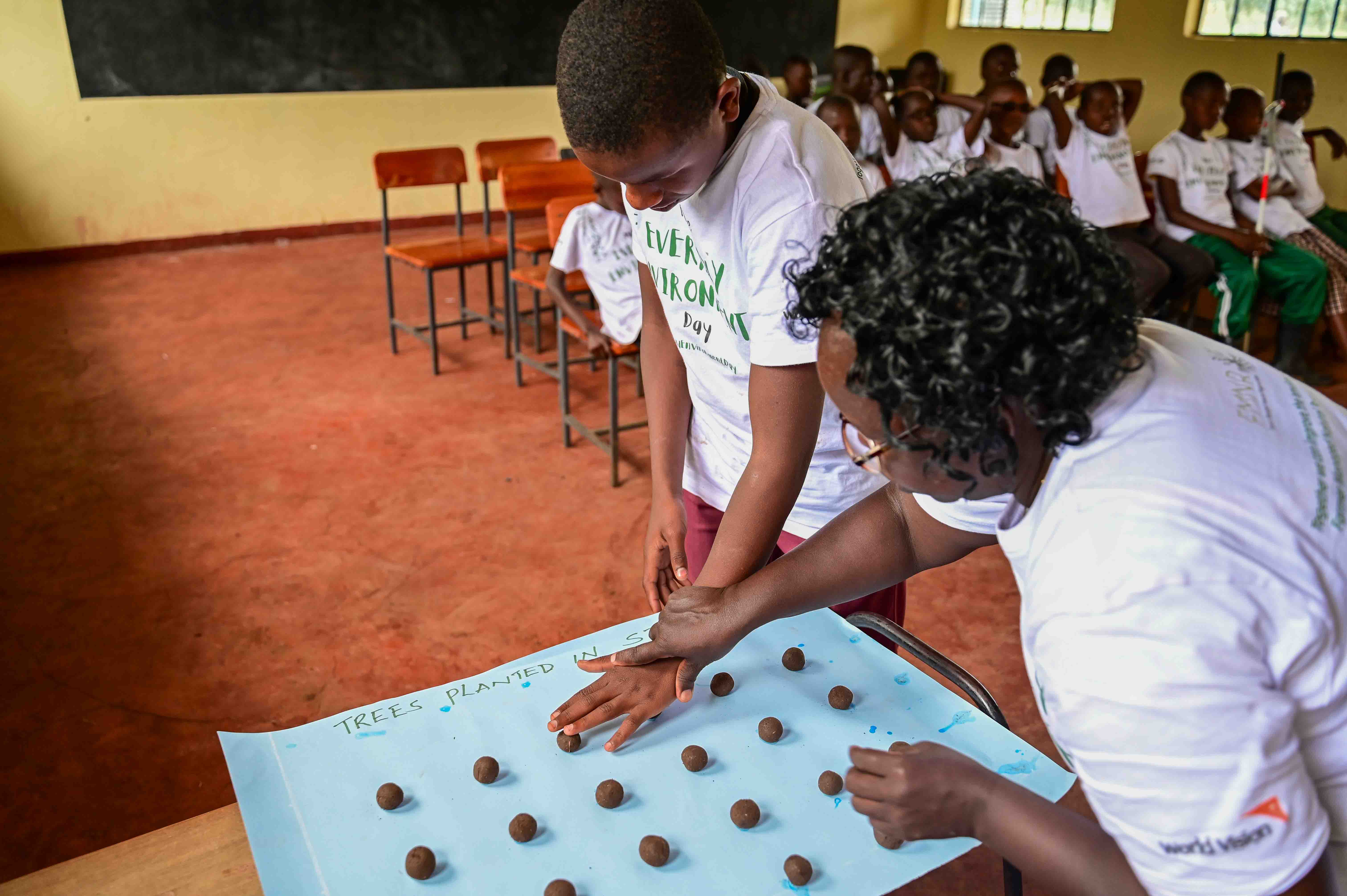 Selly, the 4K Club patron teaching a student about recommended spacing when planting trees using his sense of touch. ©World Vision Photo/Hellen Owuor