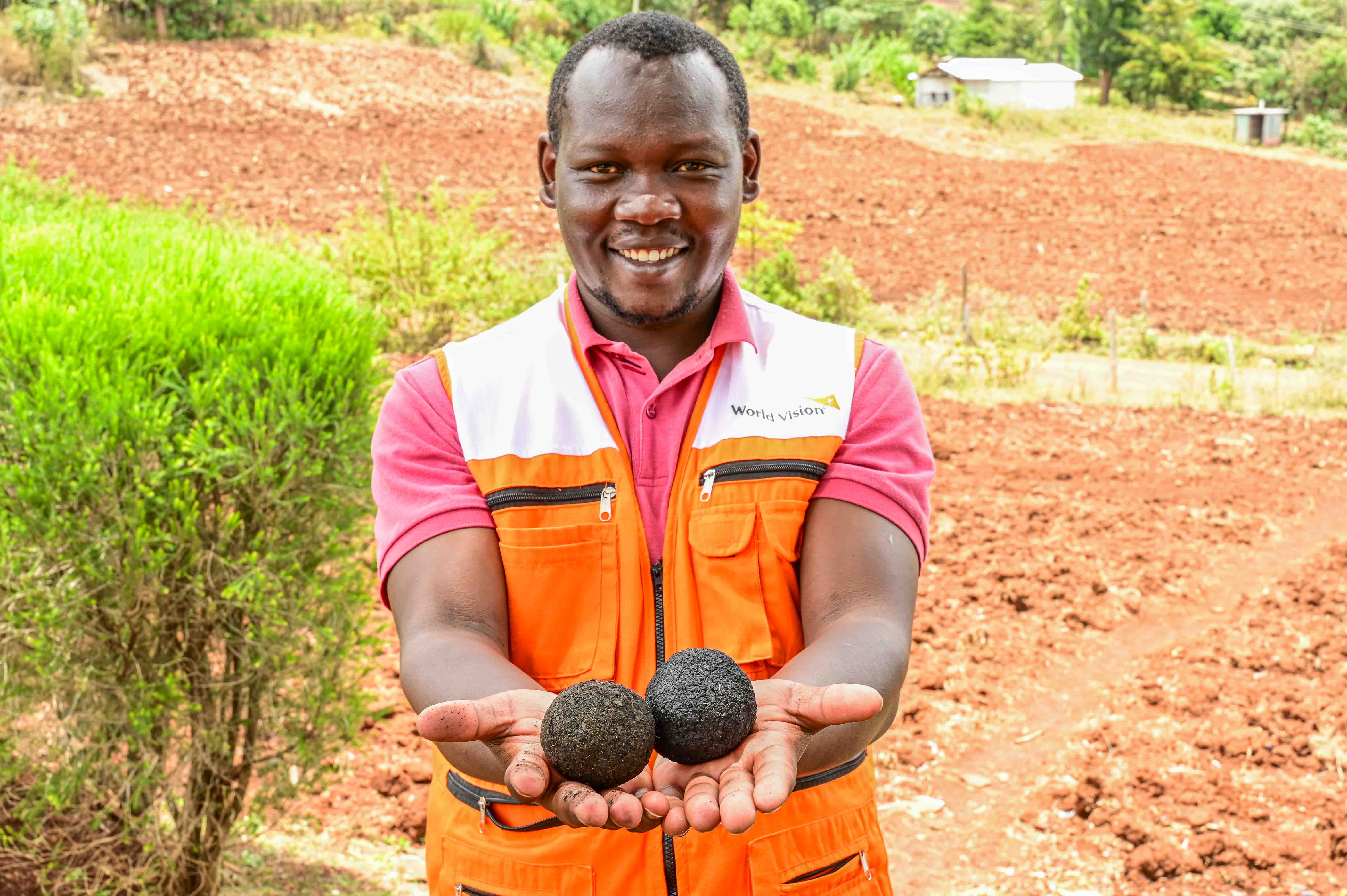 Mathew Korir, CRIFSUP Project Officer, World Vision holds a briquette made from cow dung (left) and another made from flour (right). ©World Vision Photo/ Hellen Owuor