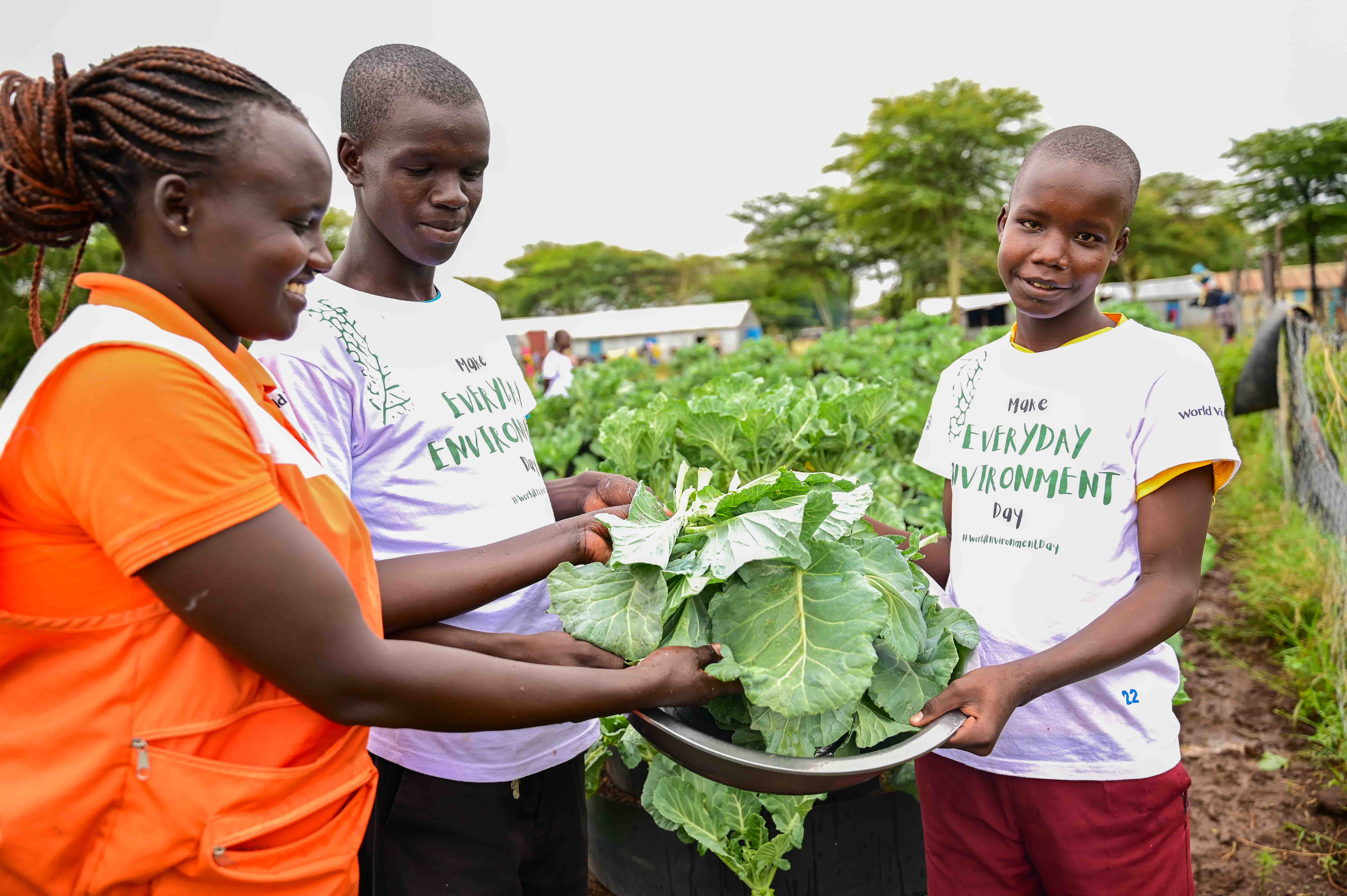 Students harvesting vegetables at their kitchen garden in the company of a World Vision staff.