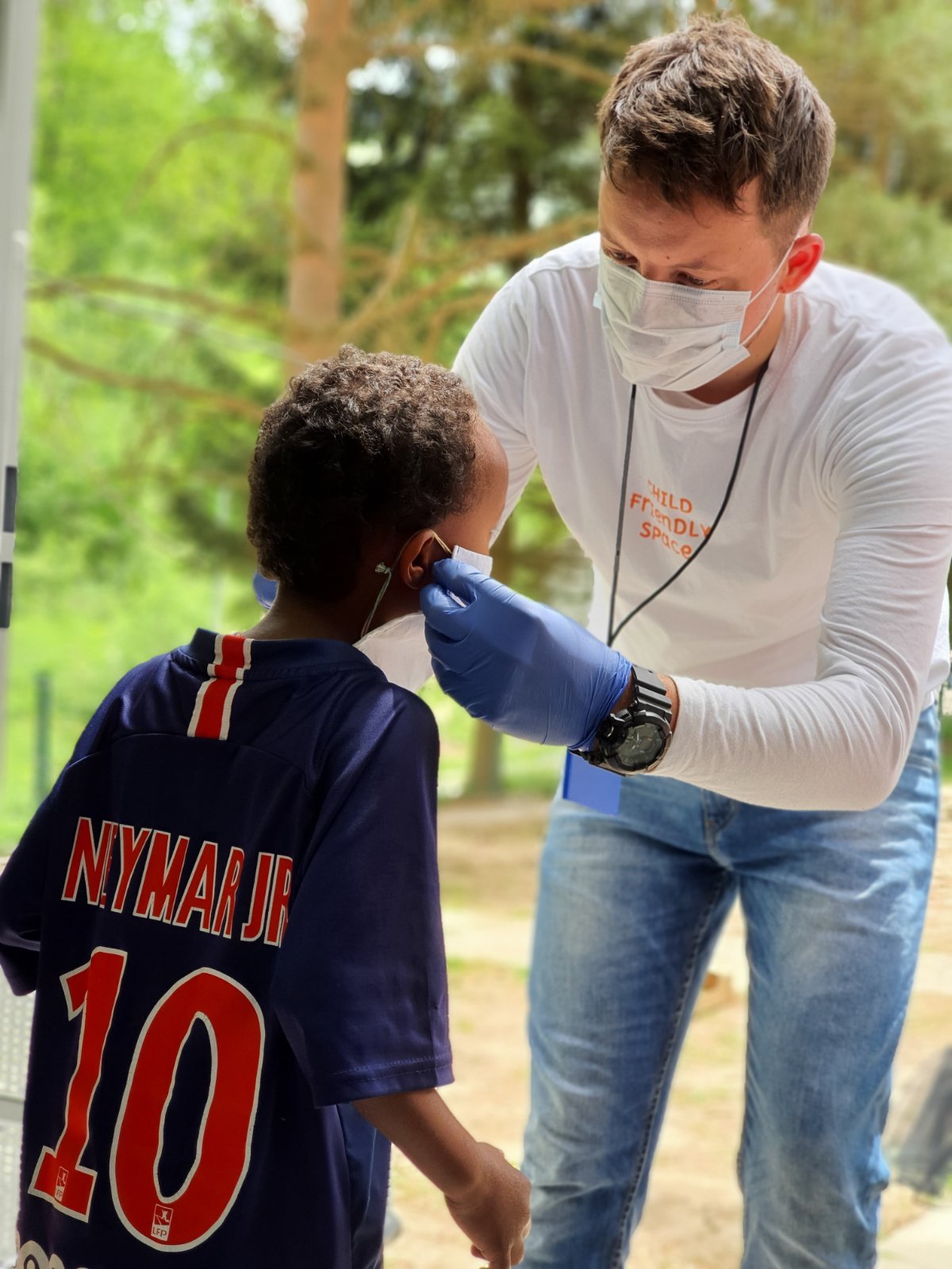 Muamer is helping a child fit the protective mask