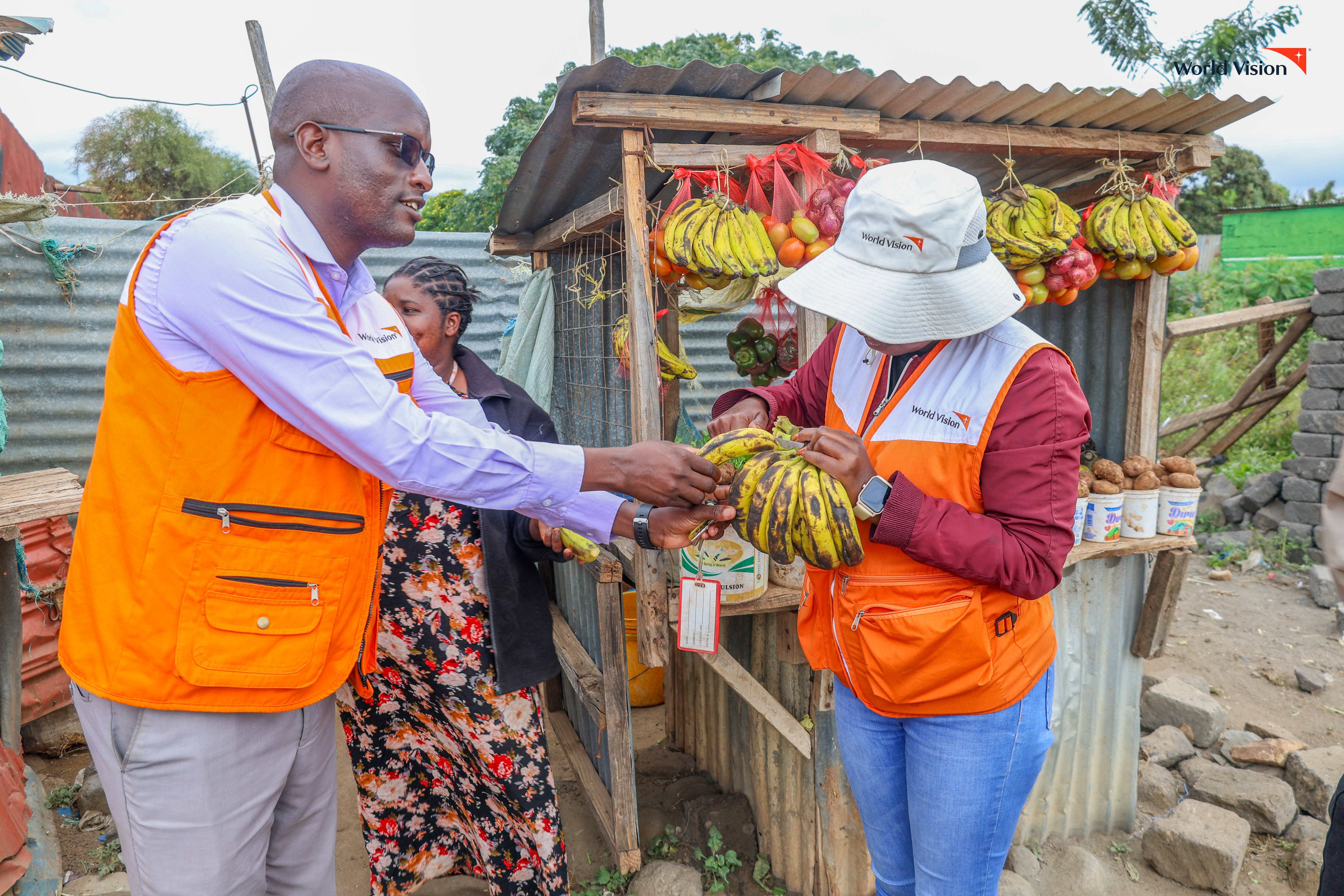 World Vision staff share a lighthearted moment at Felister’s stall, enjoying bananas from her now thriving business. ©World Vision Photo/Mirriam Kioko