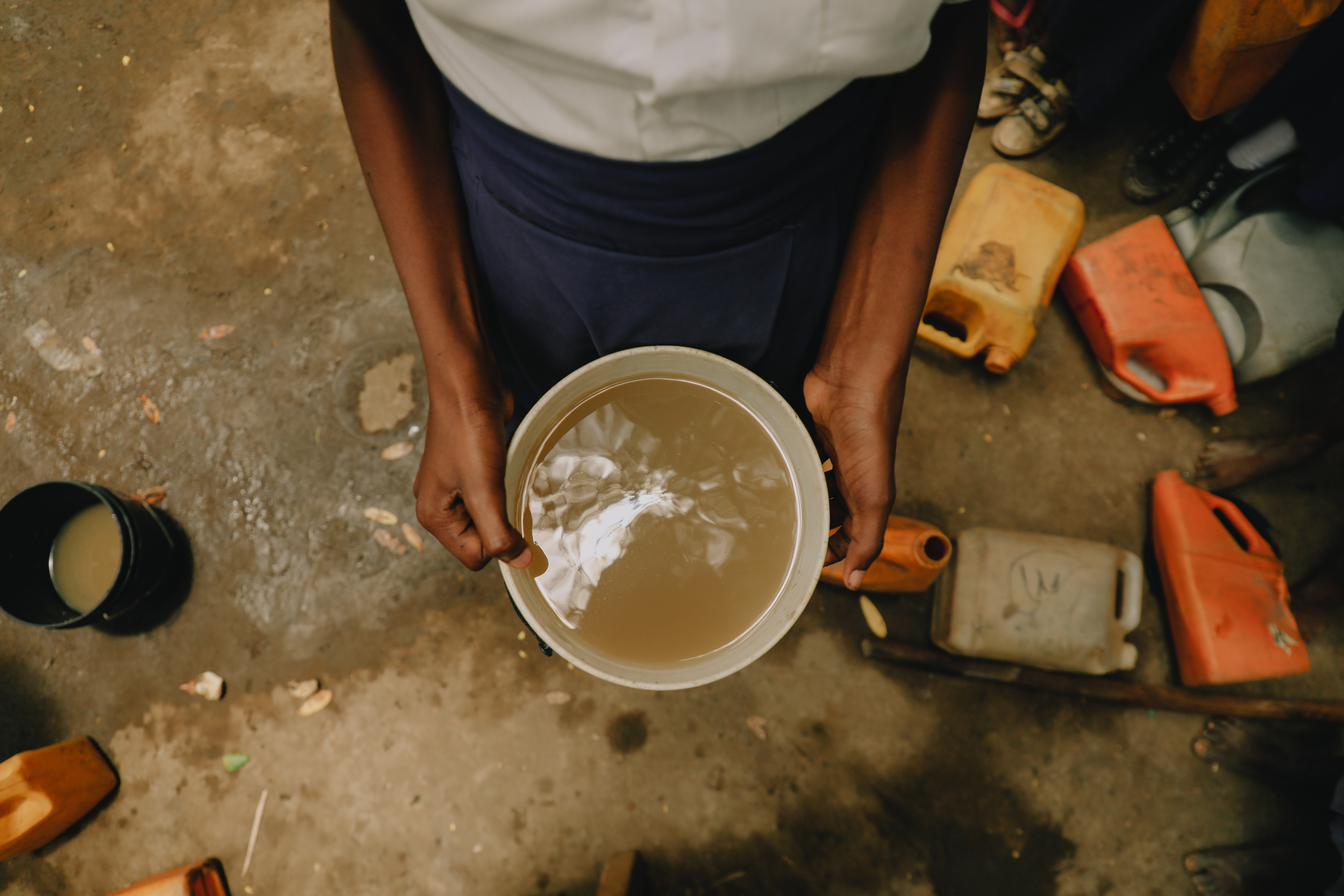 a child shows the water commonly used in the community in Tanzania. It's a murky brown.