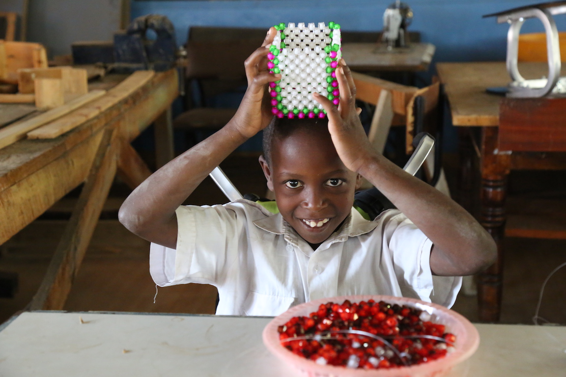 Thanks to the wheelchair, Gift is able to enjoy beadwork which is his passion. ©World Vision Photo/By Hellen Owuor.