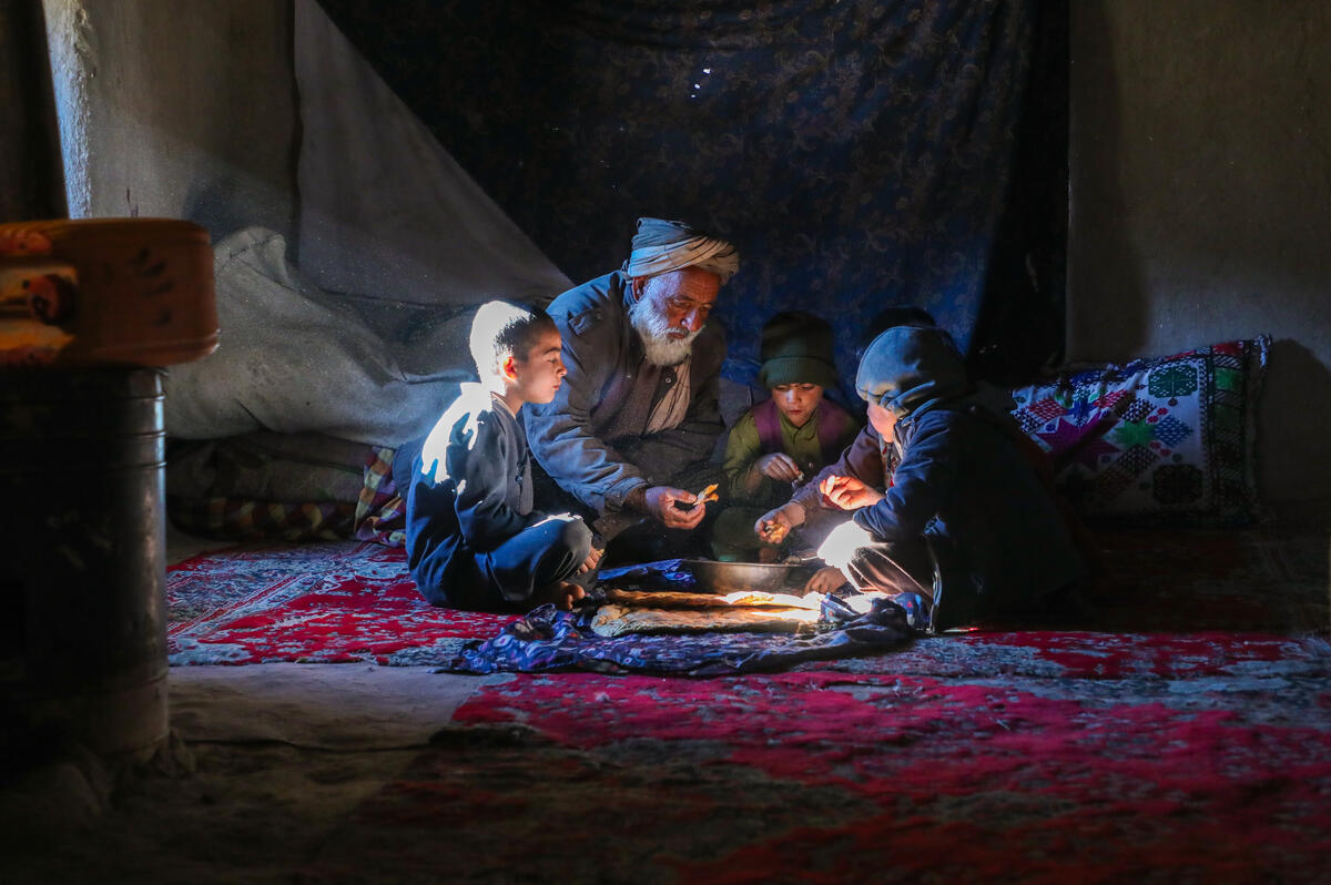 Amir, 55, and his family sitting for a meal on rugs in their home.