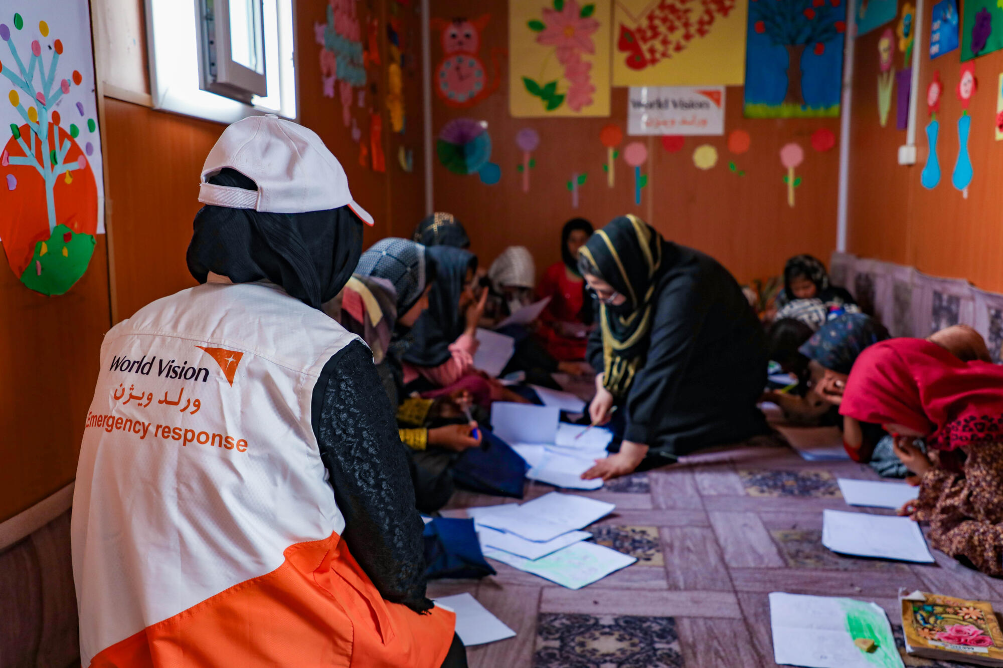 World Vision emergency response staff sit with children in a child friendly space in Afghanistan.