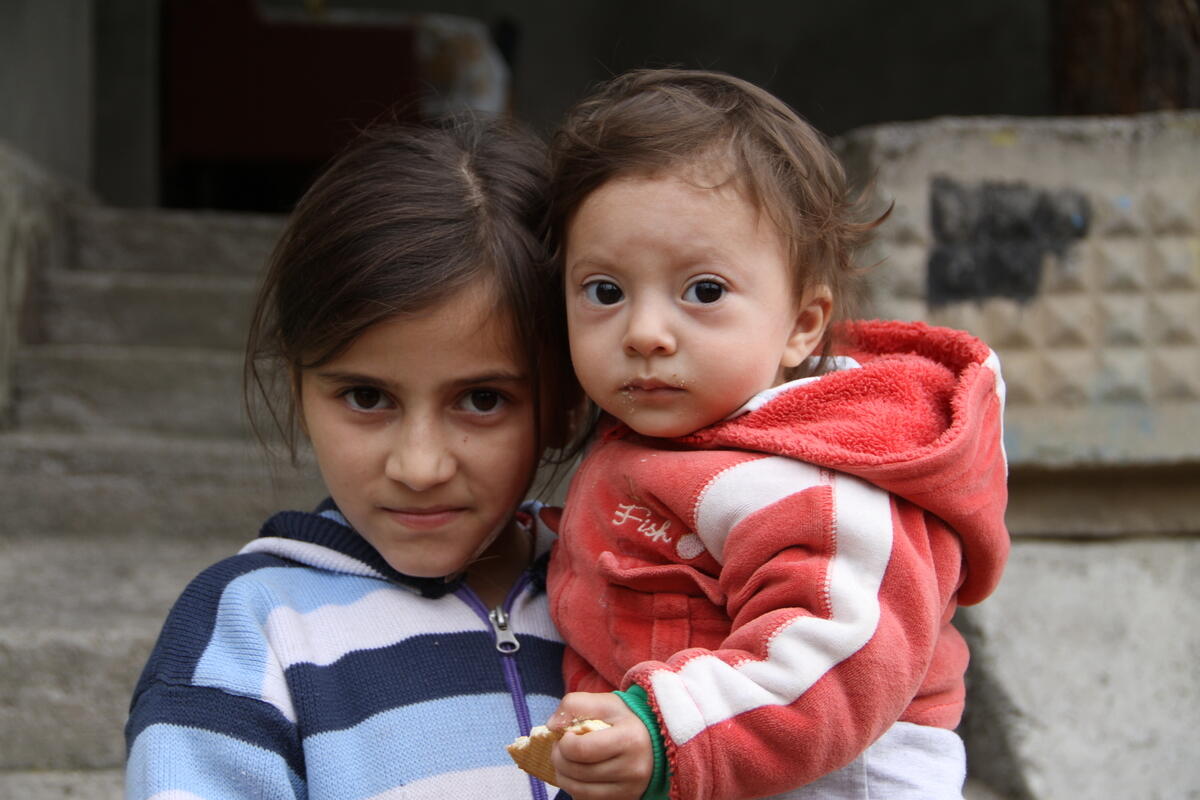 a young girl stands outside holding a baby in her ams 