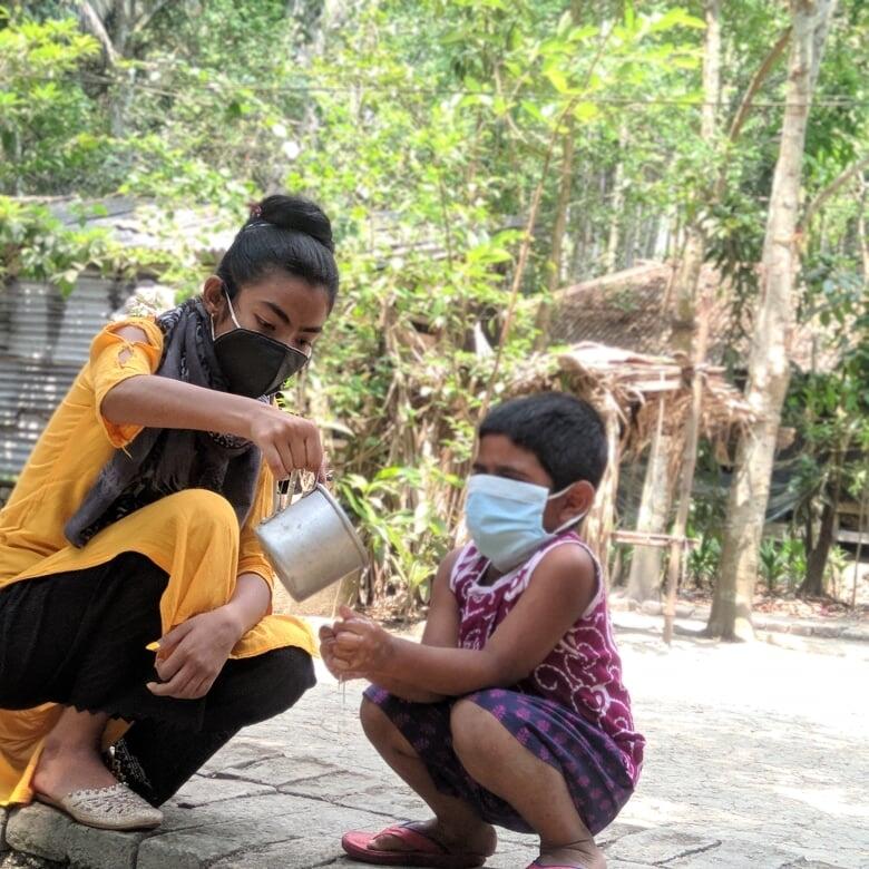 Young girl in Bangladesh helps a young boy properly wash his hands to protect himself from COVID-19