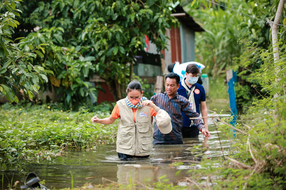 3 people wade though flood waters in Cambodia