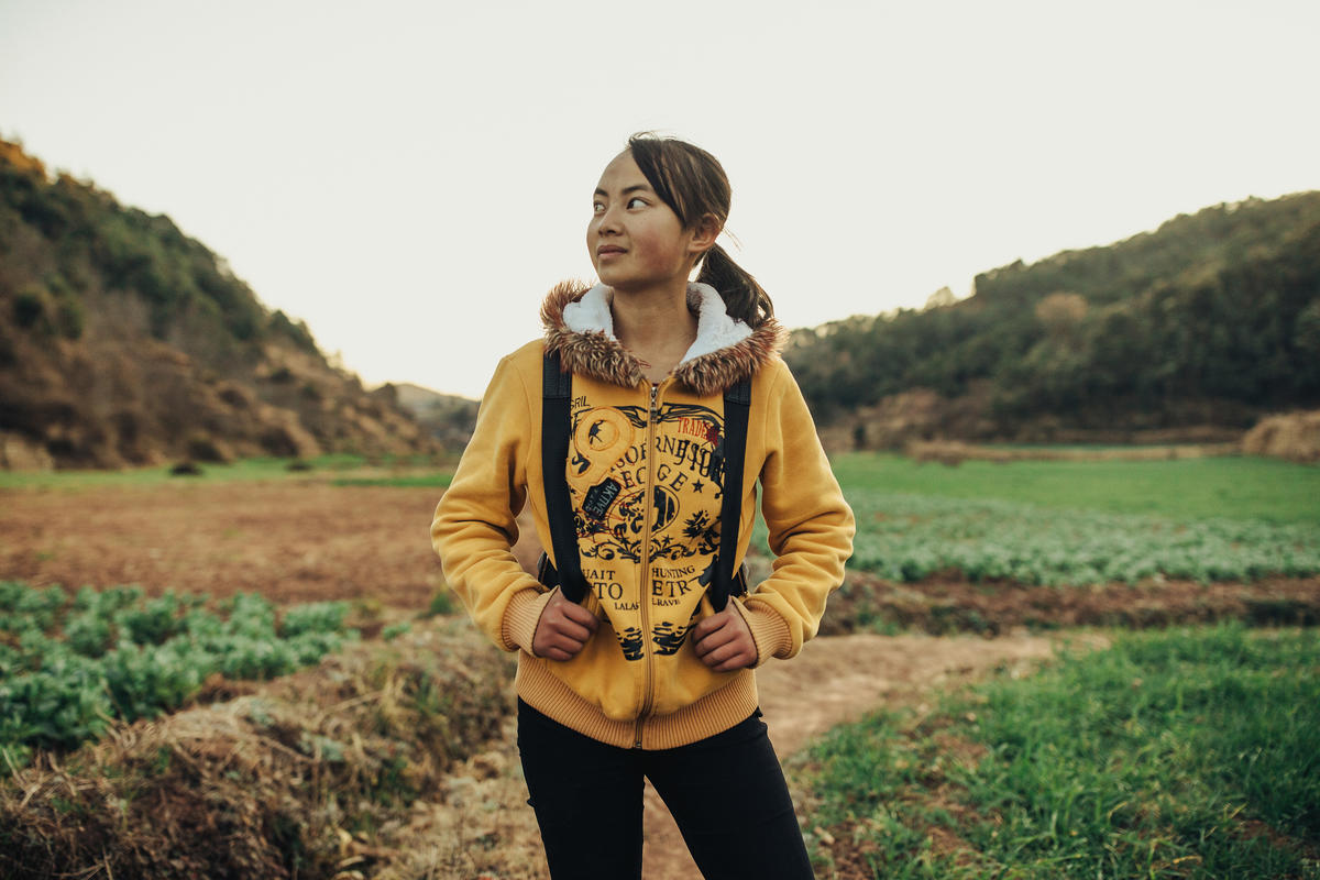 a girl stands in a field wearing a backpack