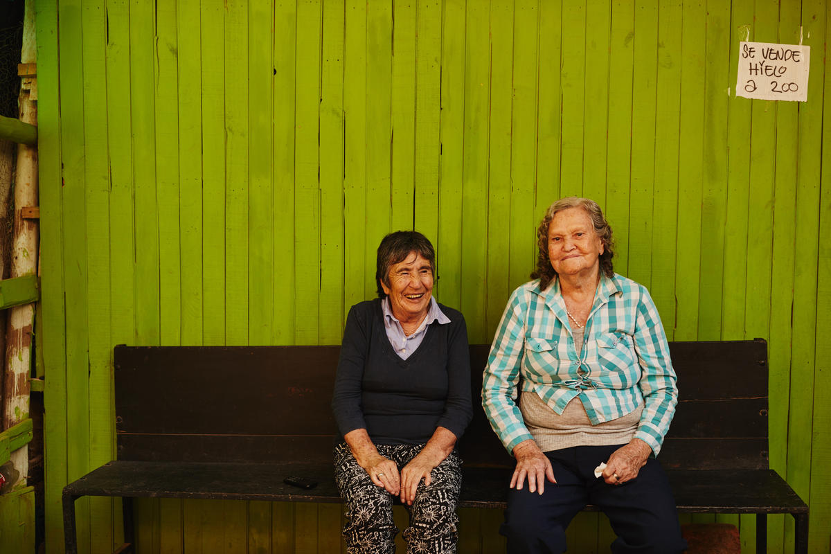 Two elderly Colombian women sitting in front of a colored wall