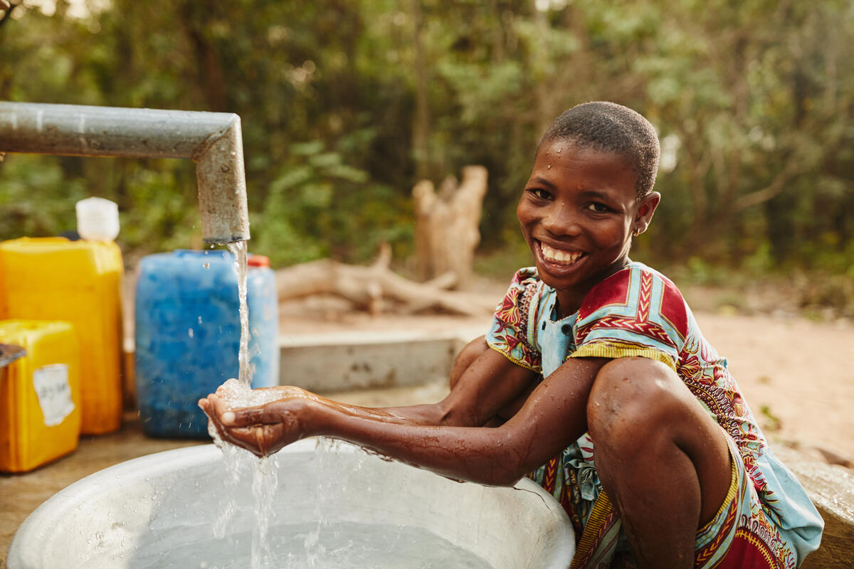 Awubanya Cecilia (wearing colored, patterned dress, sponsored), joyfully fetching water at the local water pump in Ghana