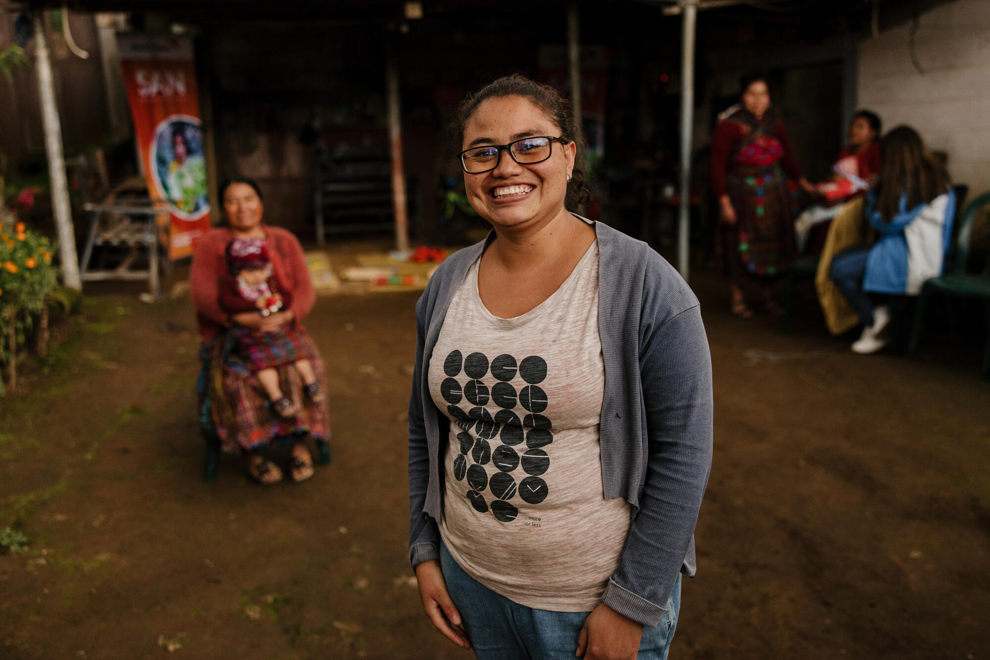 A woman stands smiling at the camera with communities members in the background.