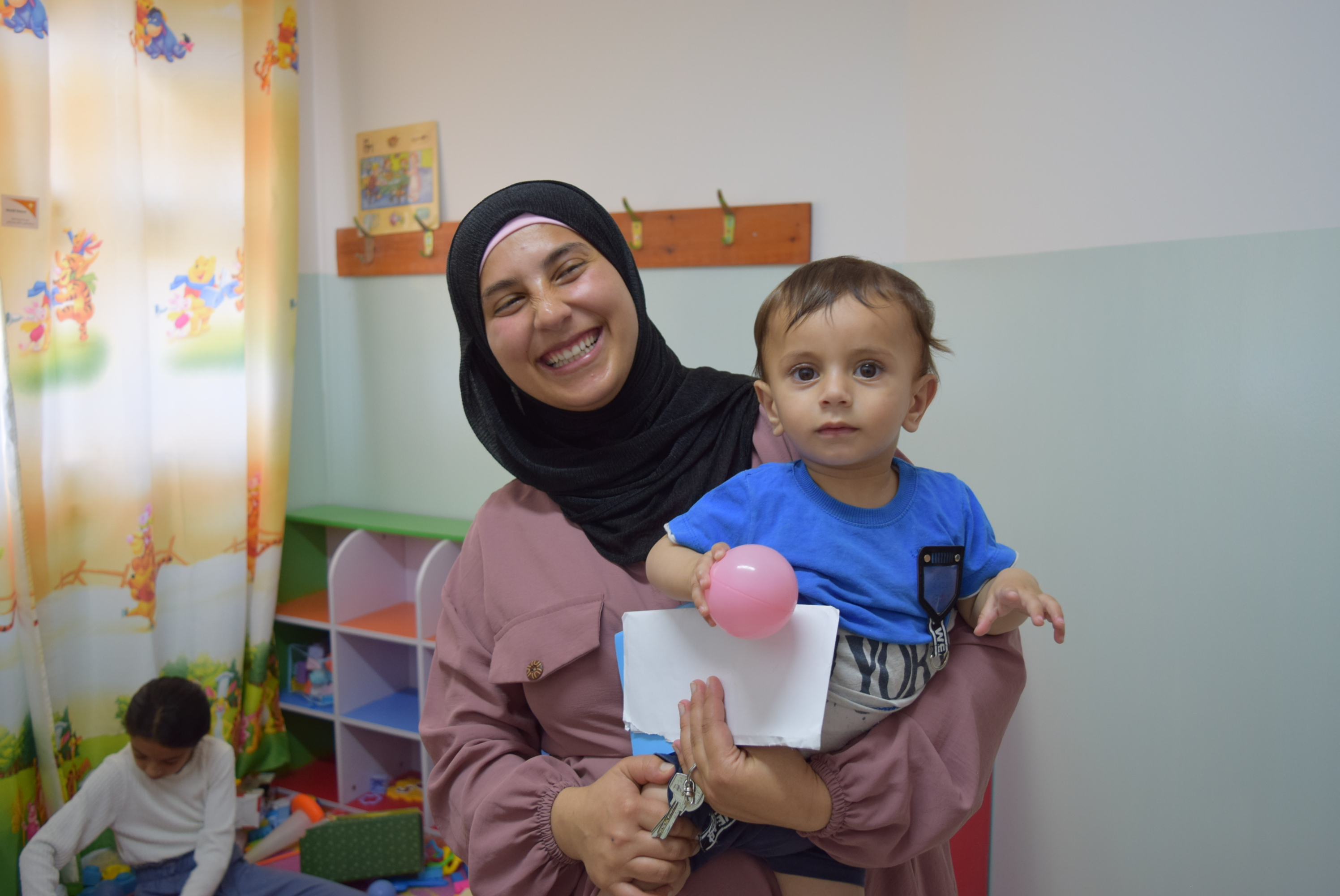 a mother holds her child in a colourful playroom designed to provide a safe and nurturing space for early childhood development.