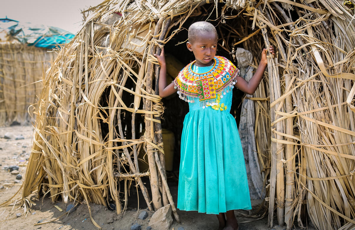 Child stands outside of entrance to hut