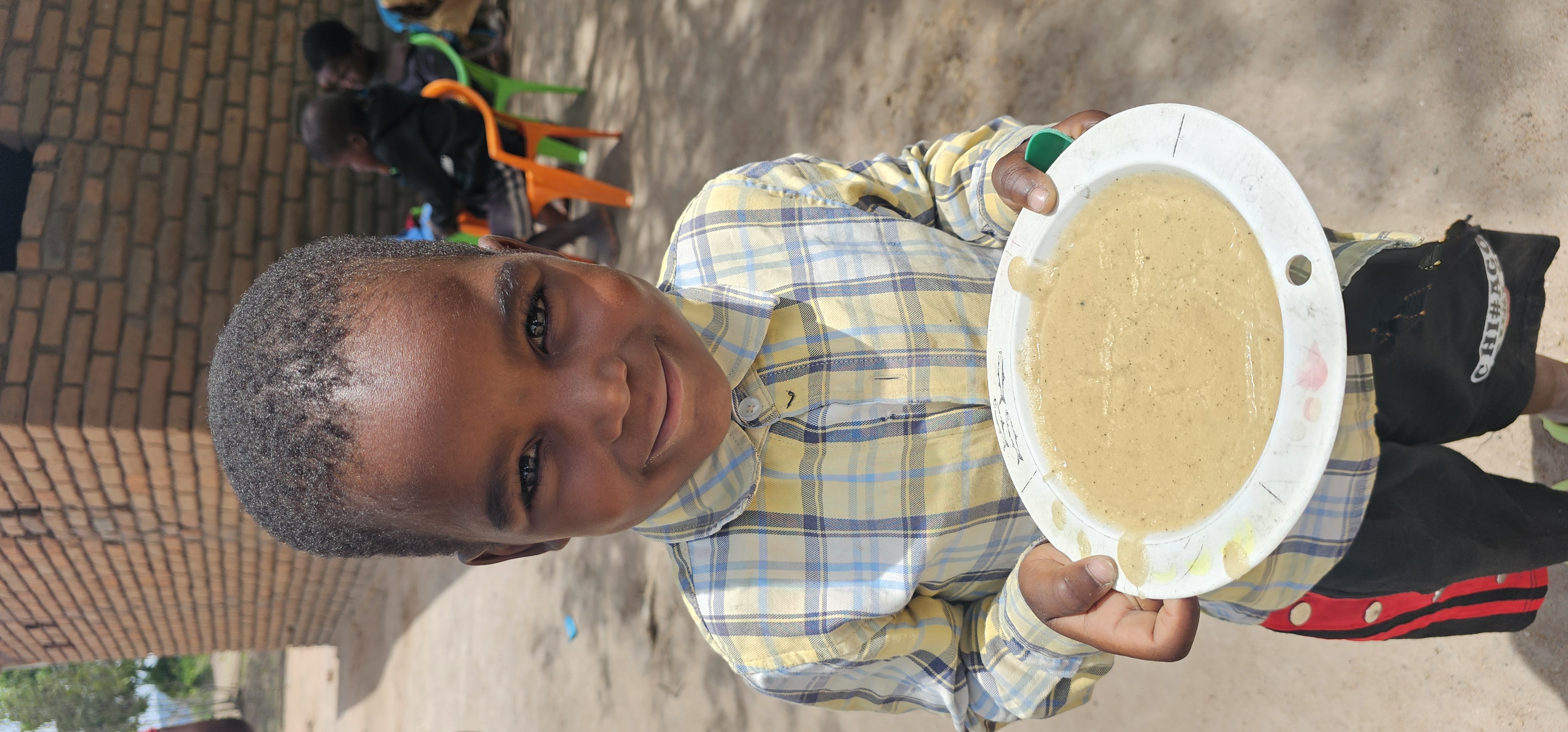Farook, a 4year old at Mfunda CBCC holding a plate of cooked Corn Soy Blend Porridge.
