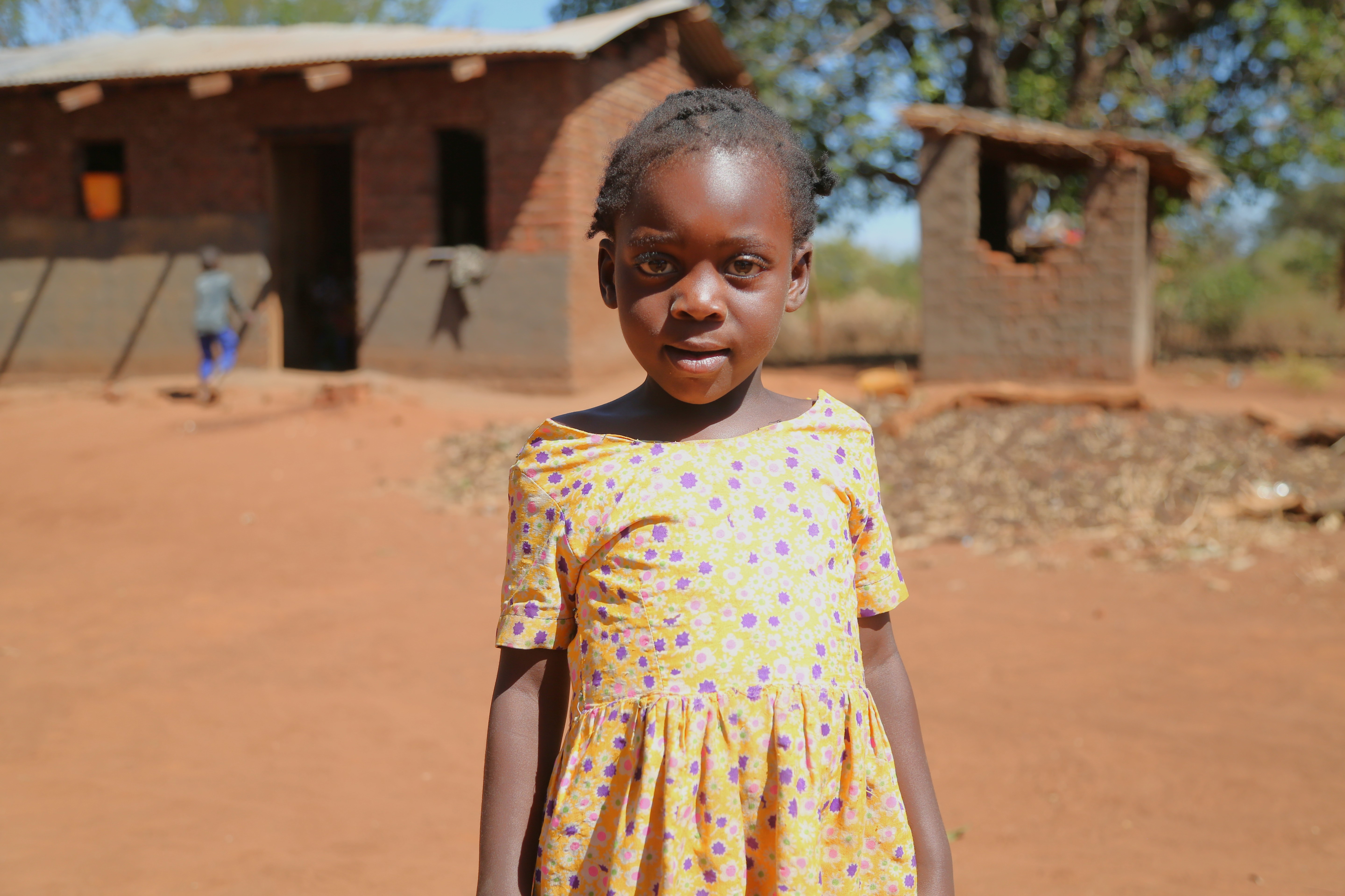 Bertha, 5, stands outside her home/ Malawi / 2025.