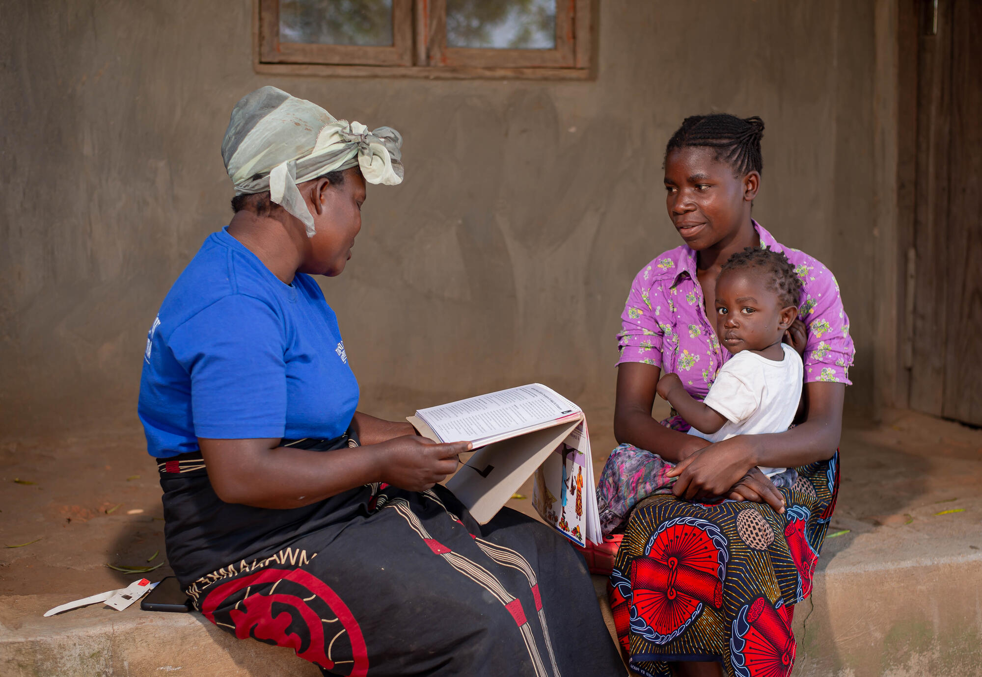 A woman sits with a mother and her child going over a pamphlet on nutritious meals