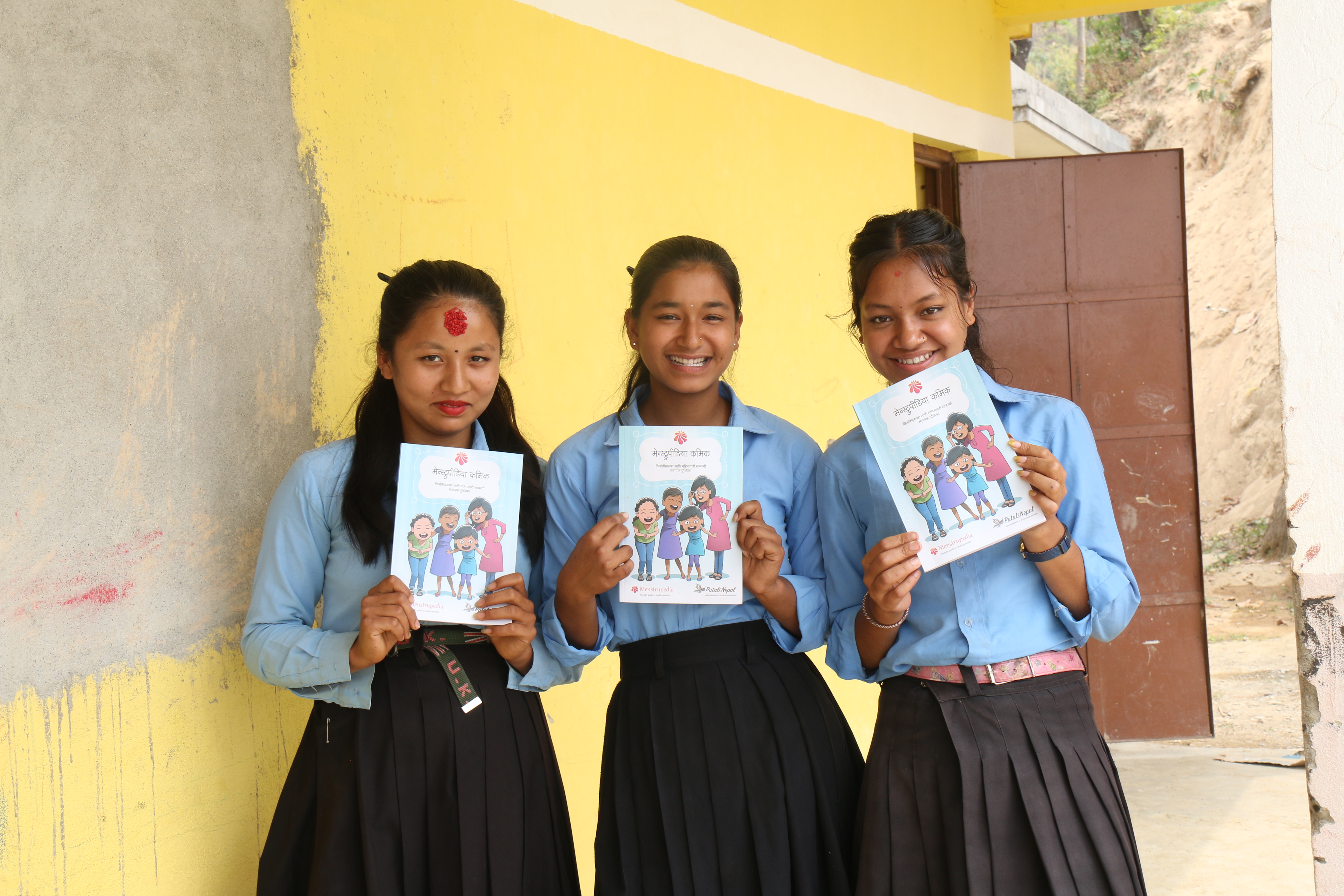Three adolescent girls from Shree Madhyamik School in Sindhuli District pose with a Menstrupedia after a Menstrual Hygiene Training