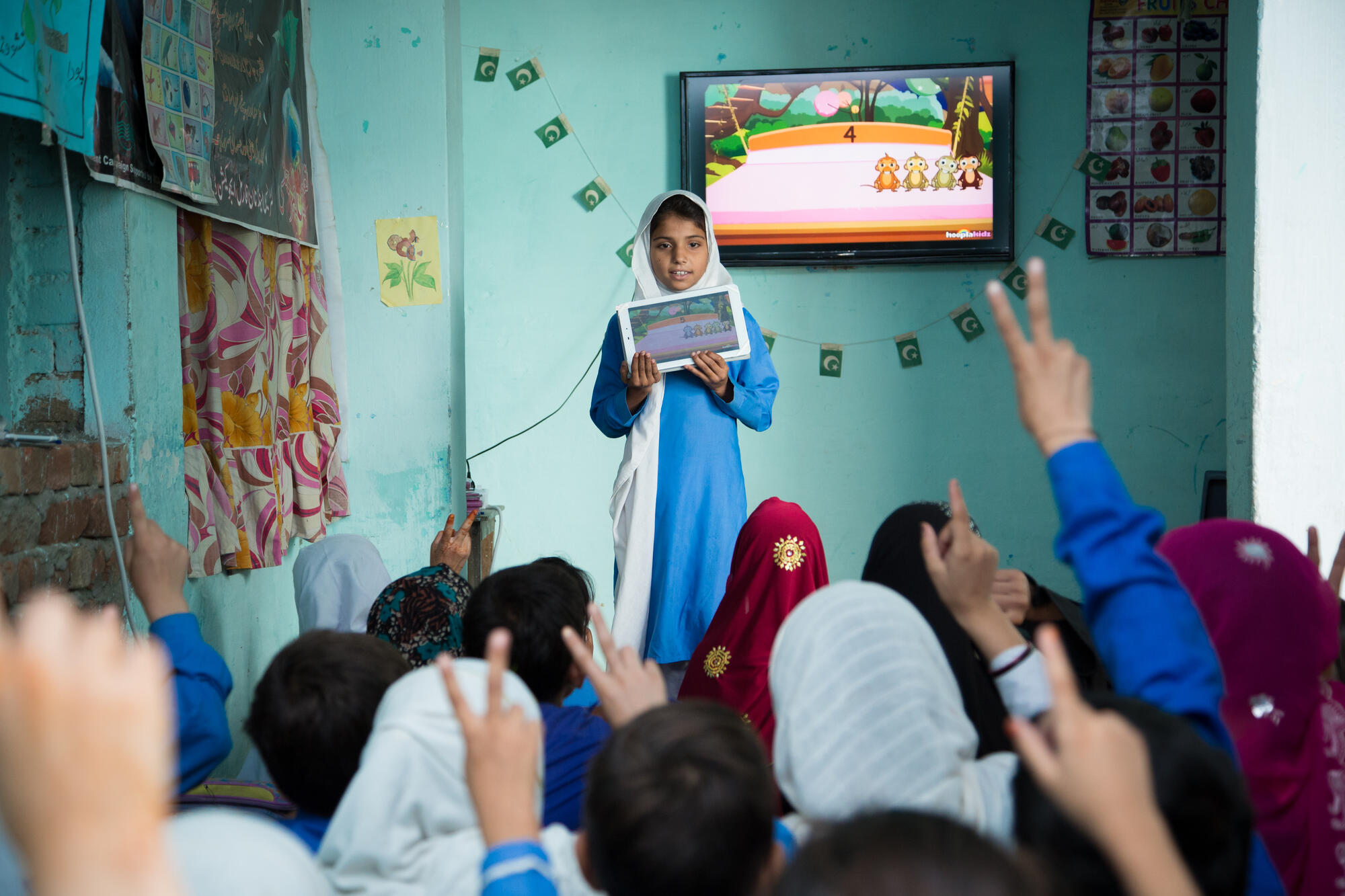 A young girl holds a tablet in front of a classroom