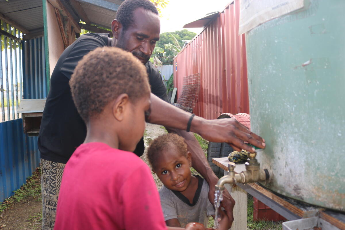 A man and his two children wash their hands at a water source.
