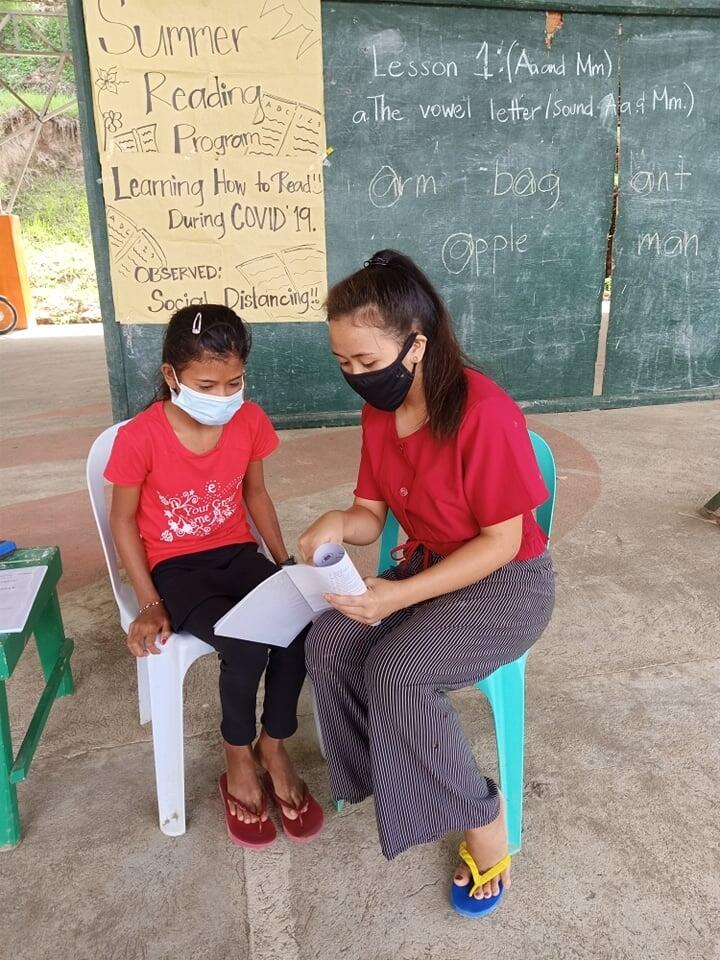 Mae teaches a younger student to read during COVID-19 lockdowns