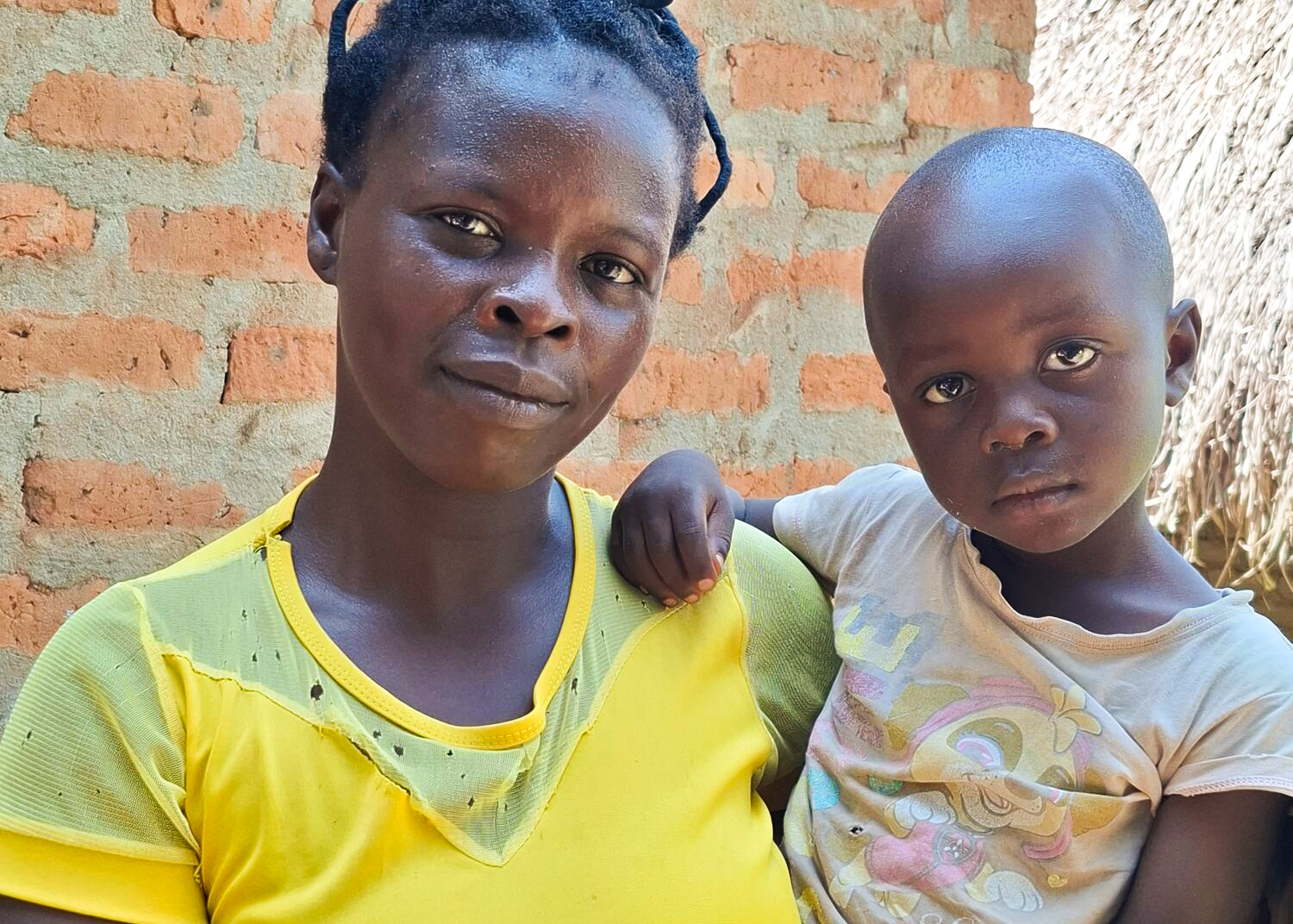 A woman in a yellow shirt hold her young child.