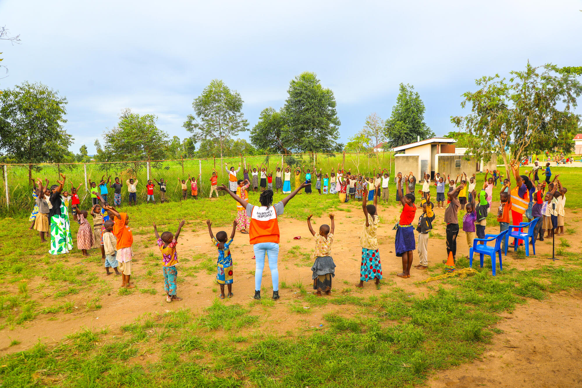 Children and staff stand in a circle outside with hands raised up.