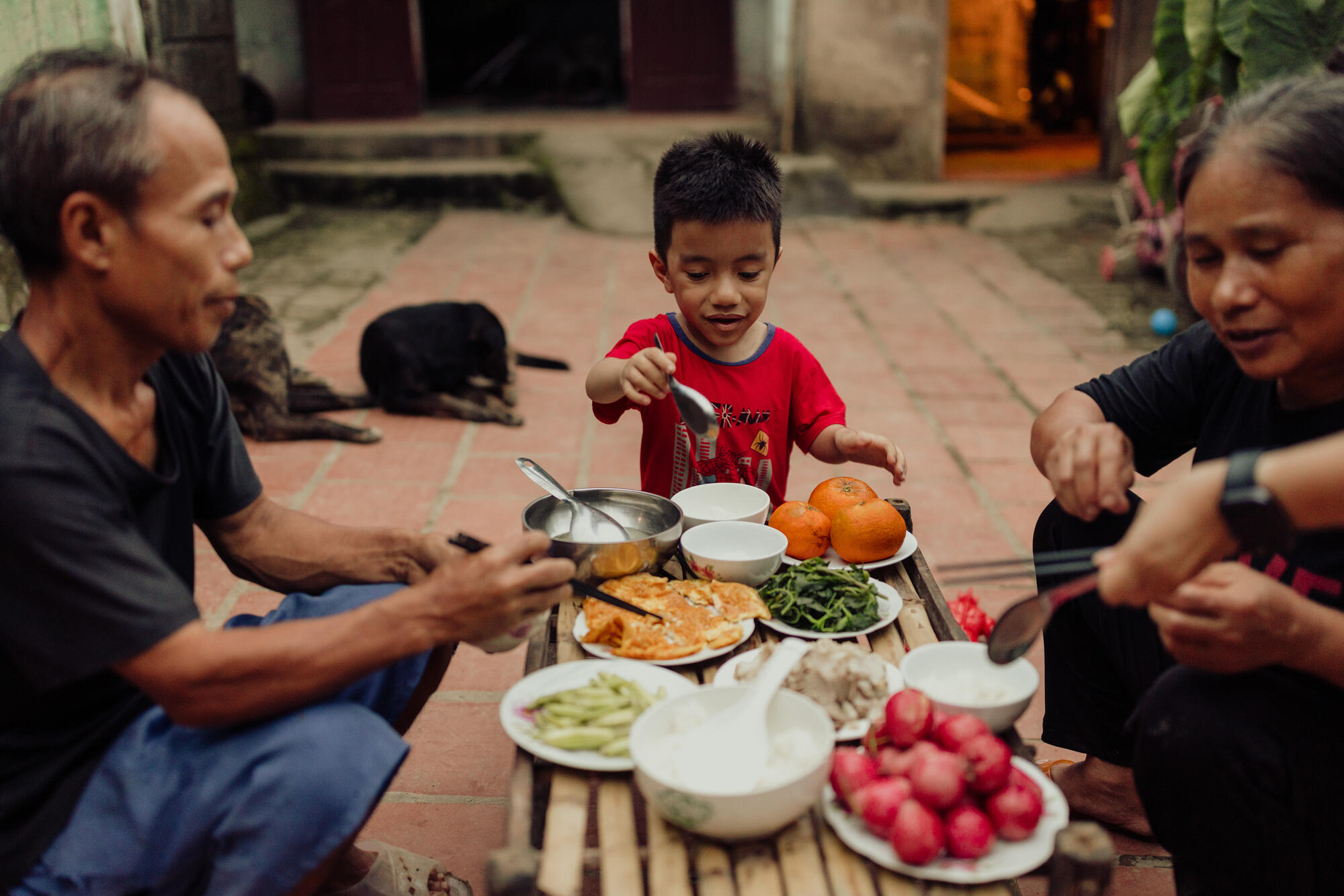 A young boy sits at a table with his parents on either side. The table is full of plates with healthy food.