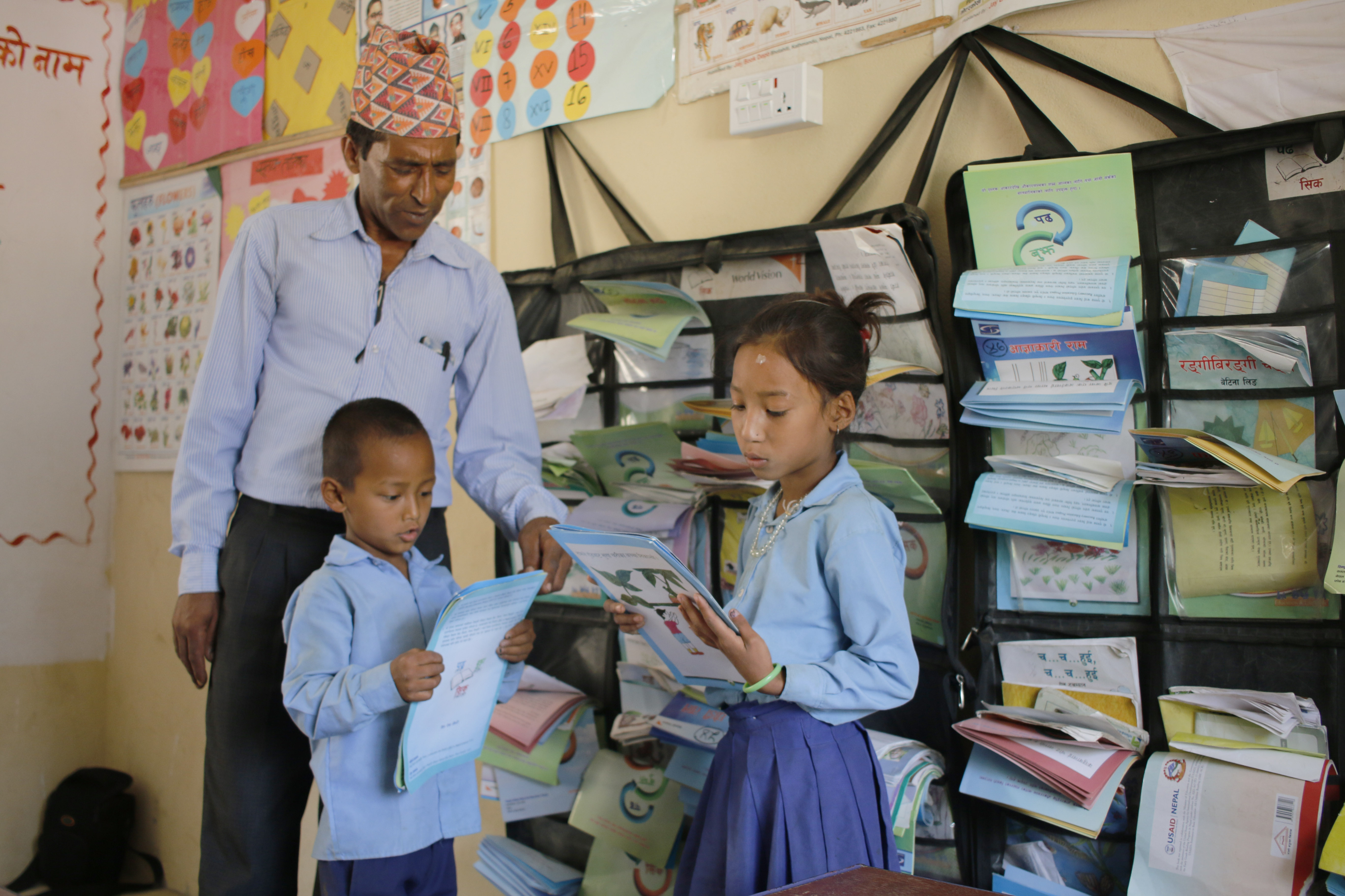 Nine year old Phadindra (boy) and eight year old Purna Kumari read books from the reading corner while Nil Prasad guides them.