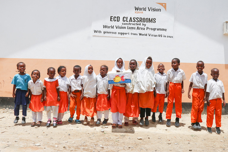 Children proudly showcase an art project outside their newly constructed classroom, made possible through the support of World Vision in Lamu, Kenya. ©World Vision Photo/Martin Muluka.