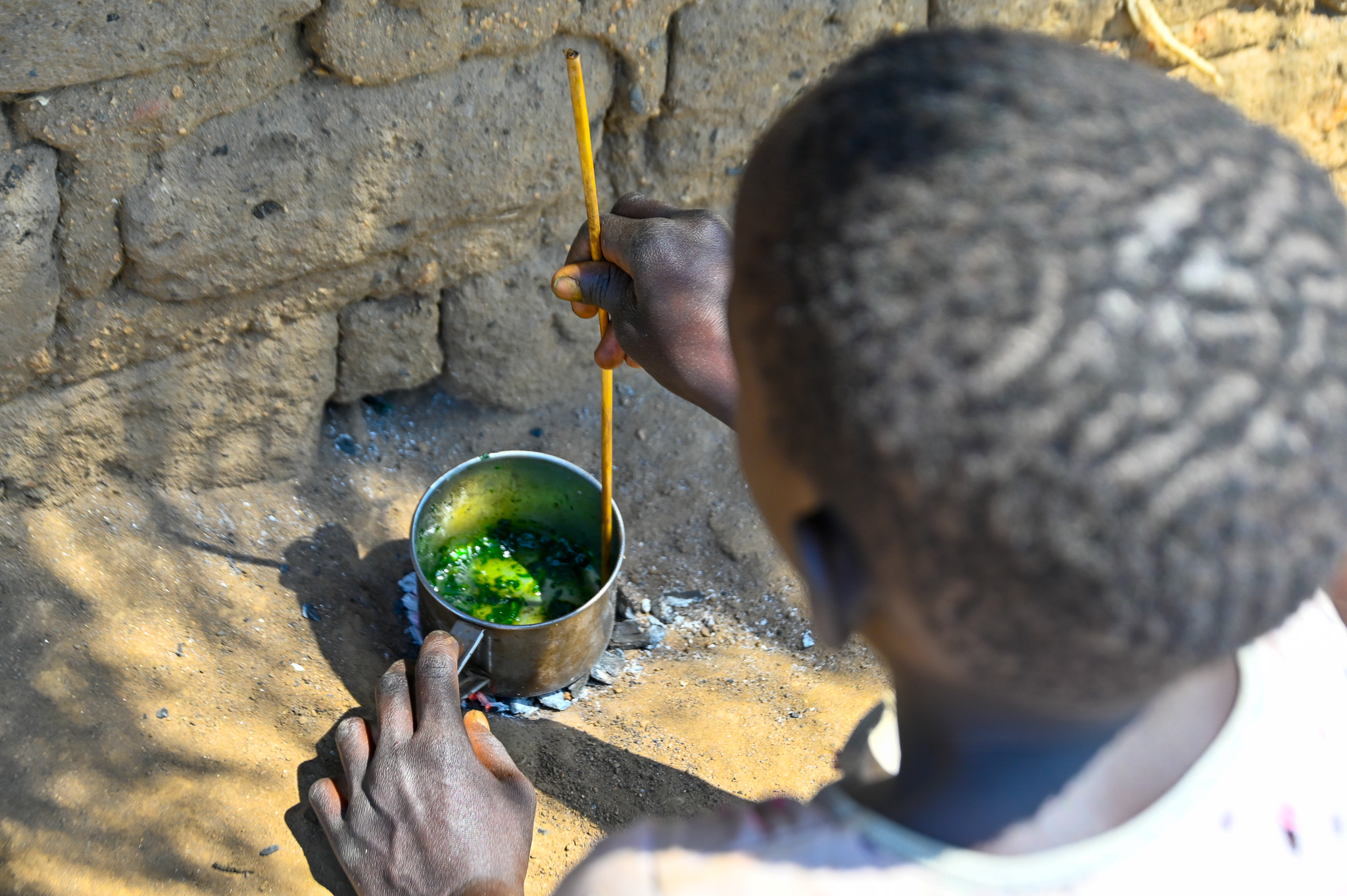 Nensa mixing a few edible leaves and water her attempt to make a meal. © World Vision Photo/Mungu Jakisa Brian