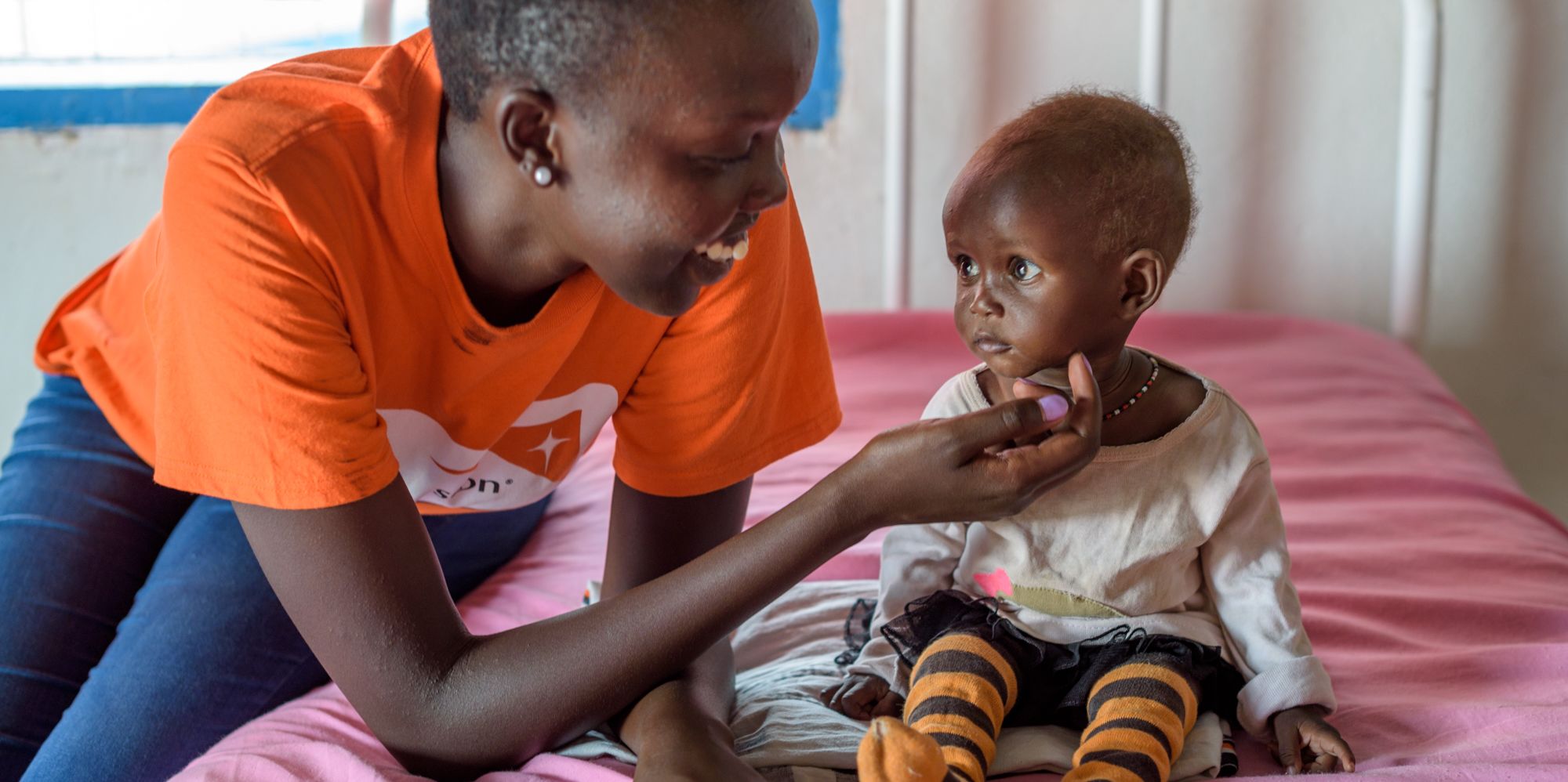 <alt="World Vision staff helping malnourished child">