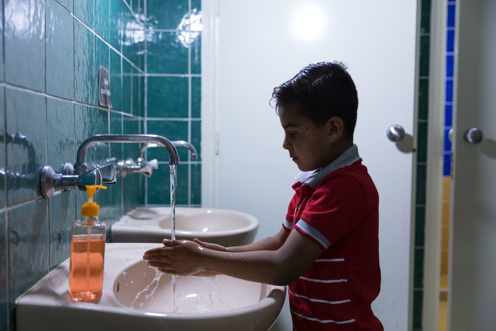 Boy washing hands at sink.