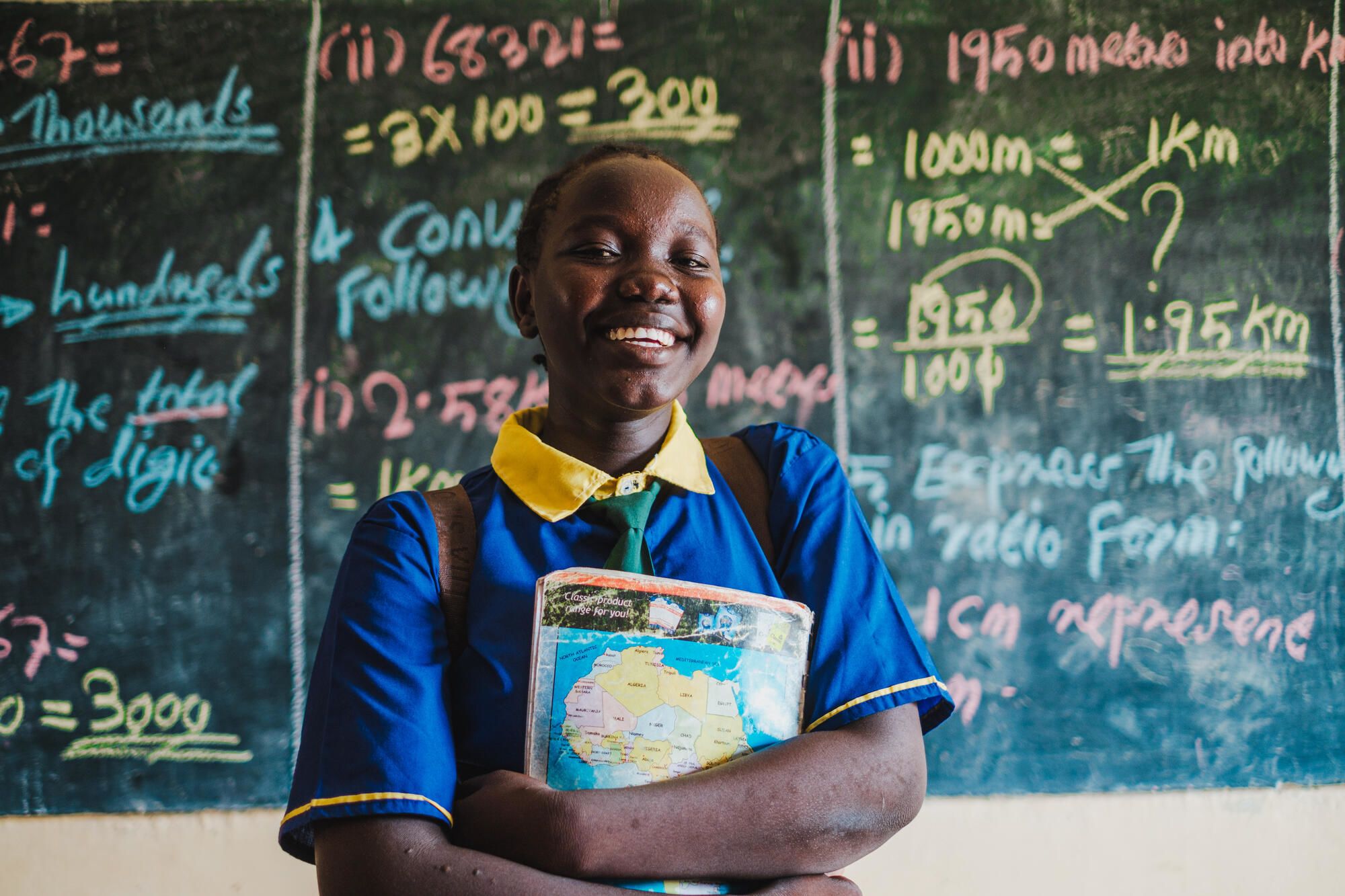 Proud teen student holding a textbook in front of the chalkboard