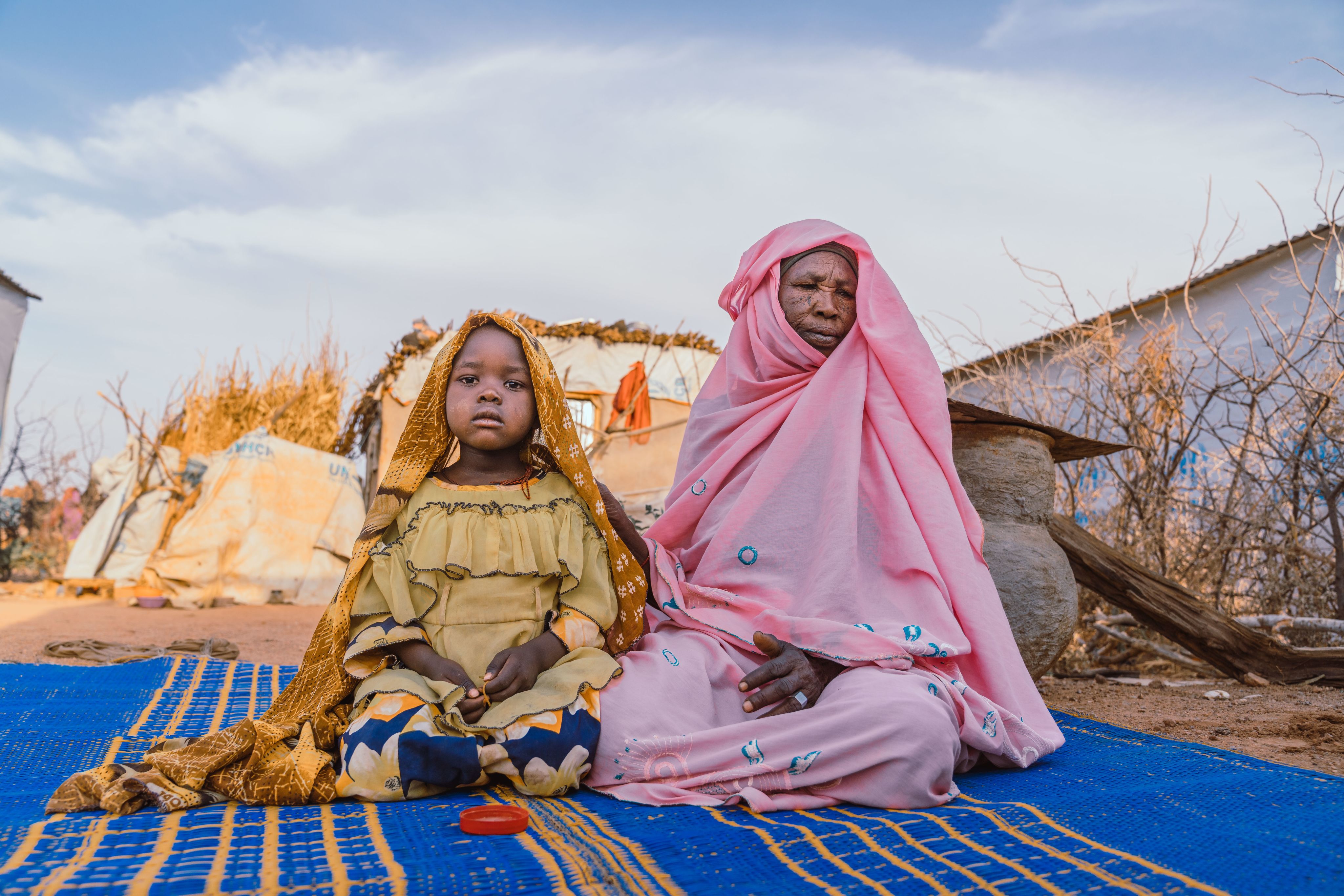 Young girl sitting on the ground with an older family member at a refugee camp