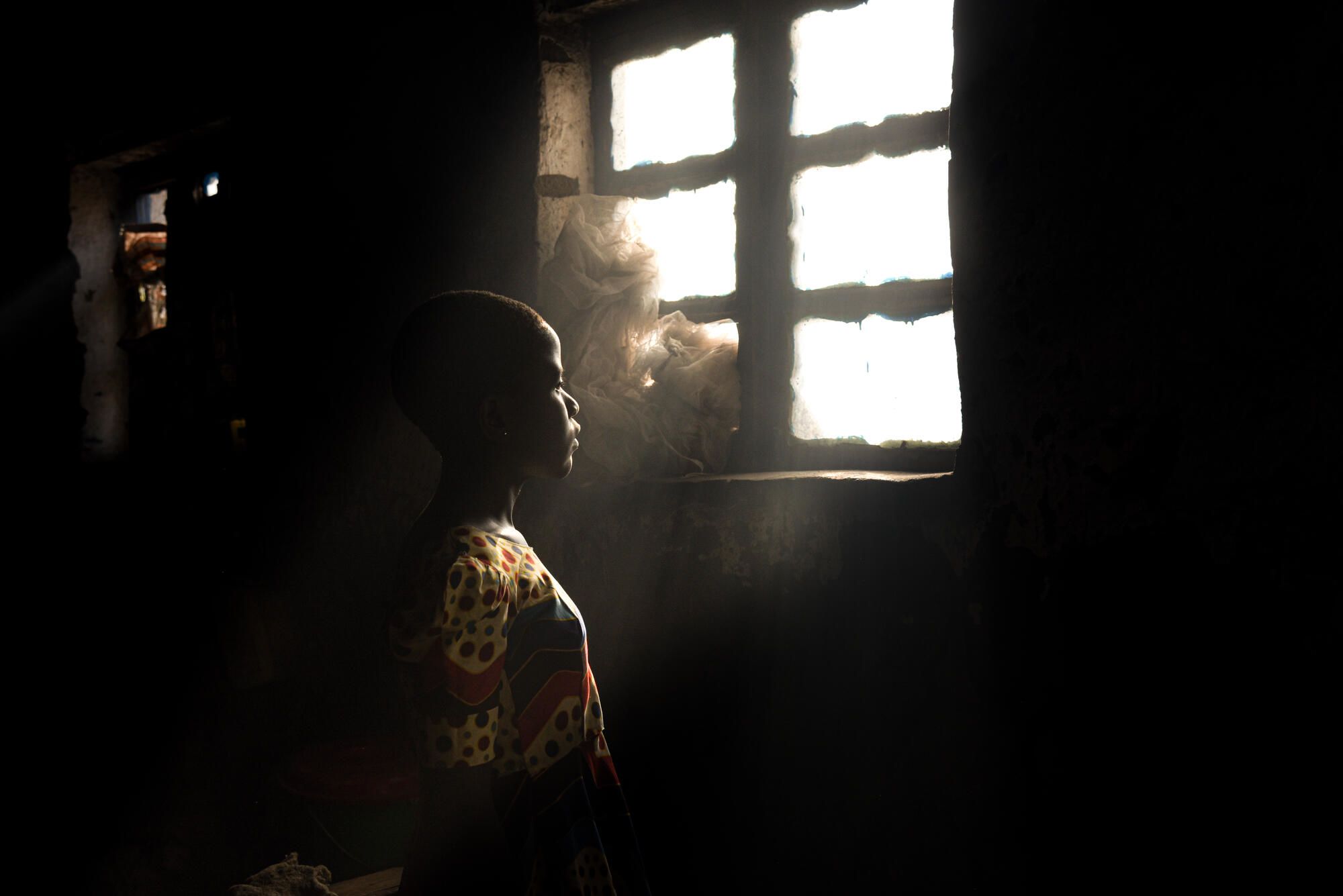 Girl standing in a dark room, looking towards the light in the window