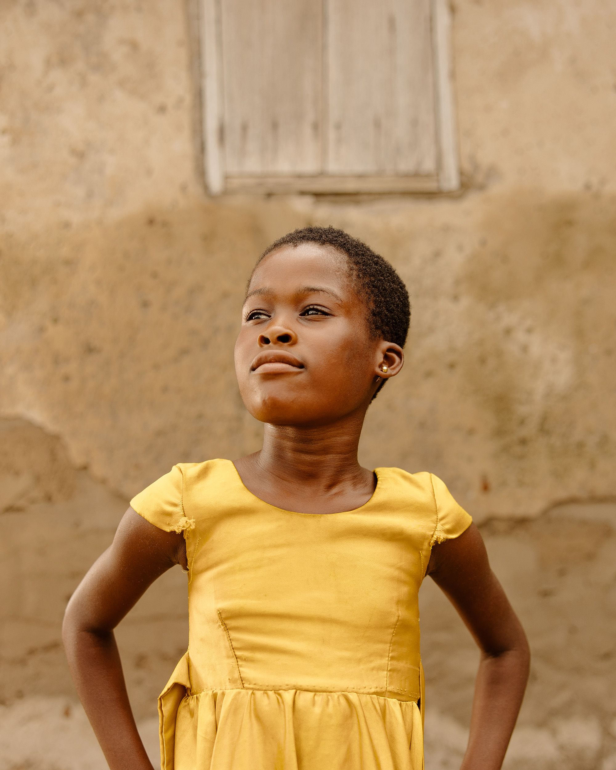 A girl in a yellow dress stands strong with hands on hips