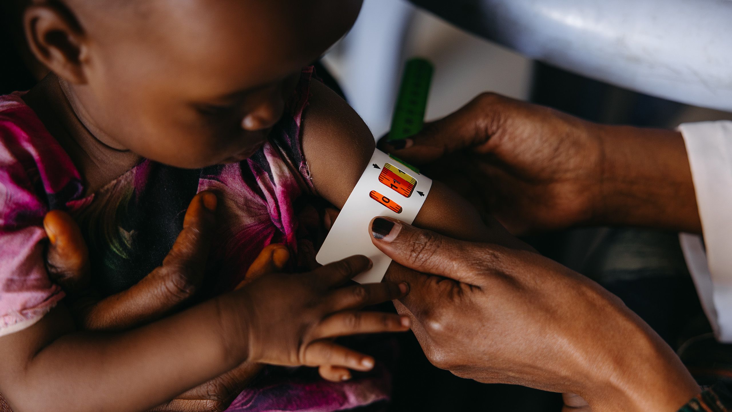 A child looks down at her arm where a health worker wraps a malnutrition measuring tape